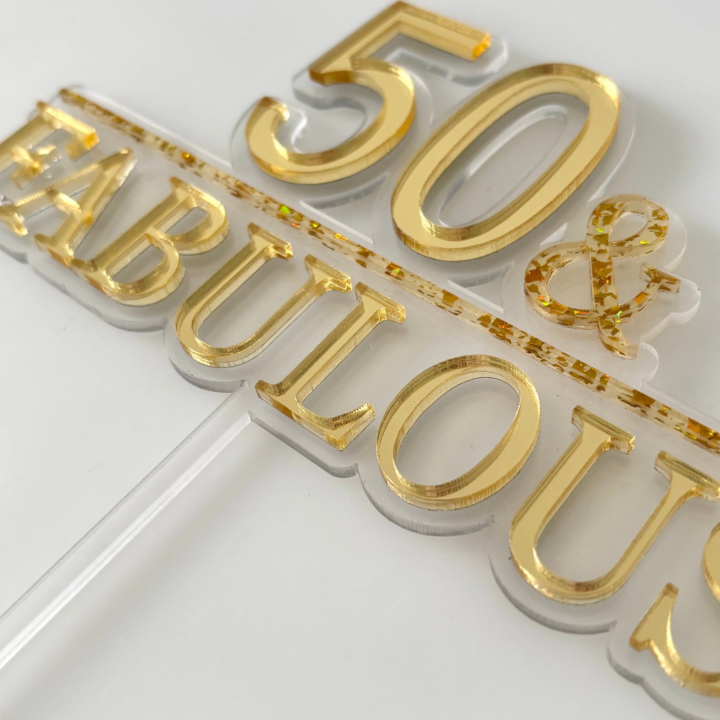 Gold and white '50 & Fabulous' cake topper on a white background