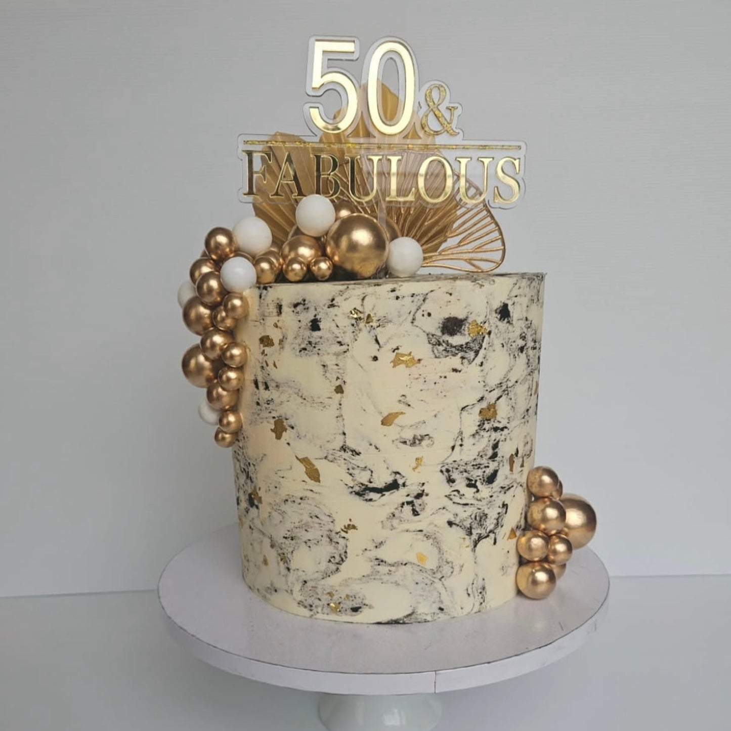 Decorative cake with gold accents and '50 & Fabulous' cake topper on a white background
