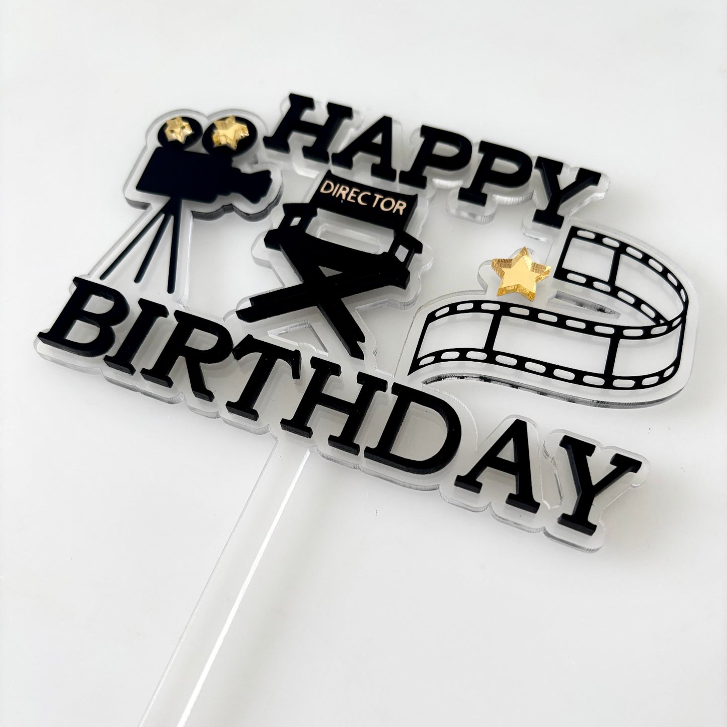 Cake topper with 'Happy Birthday' text and film reel, camera, and star icons on a white background.