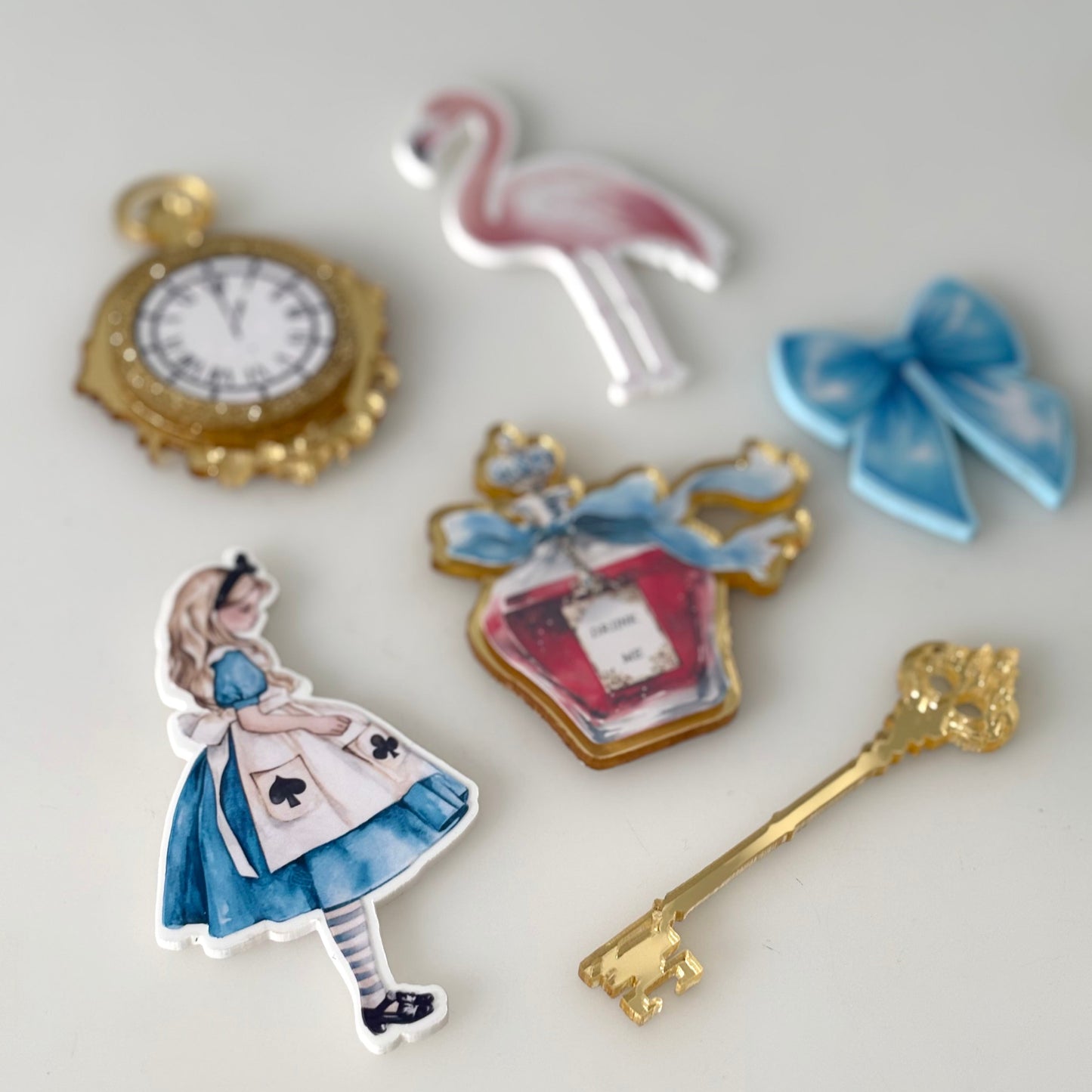 Set of decorative cake toppers including a flamingo, clock, and Alice in Wonderland-themed designs on a light background.