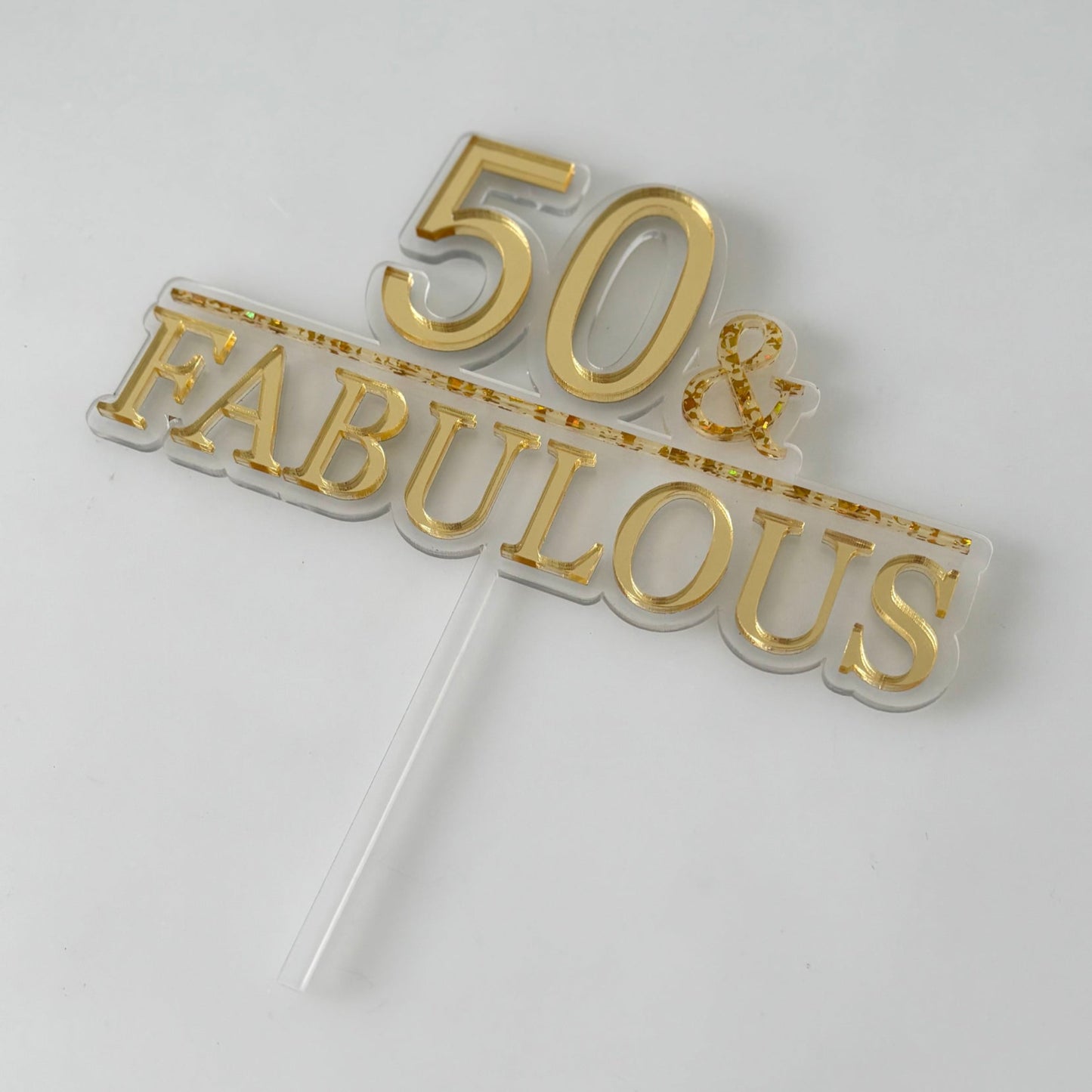 Gold '50 & Fabulous' cake topper on a white background