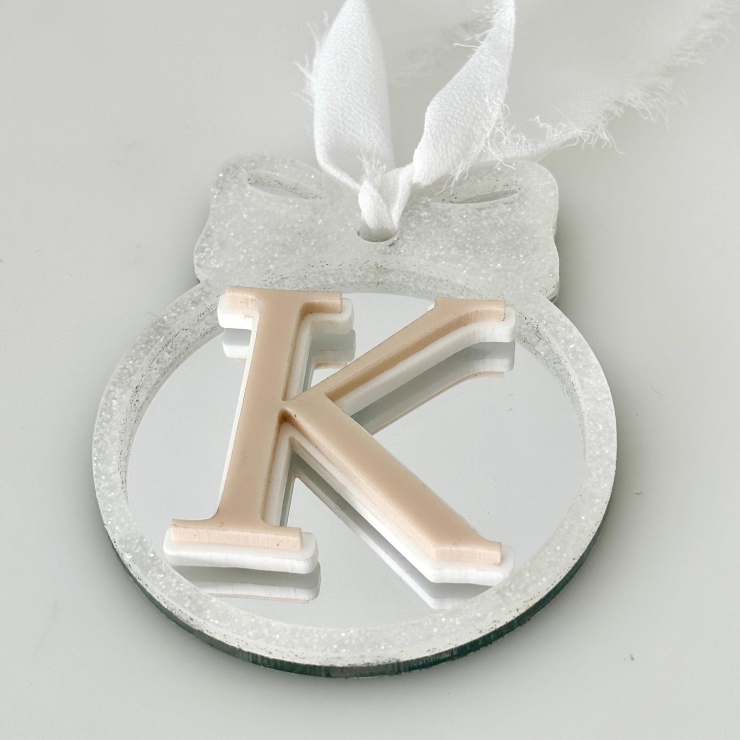 Decorative letter 'K' on a round mirror with a white ribbon against a light gray background