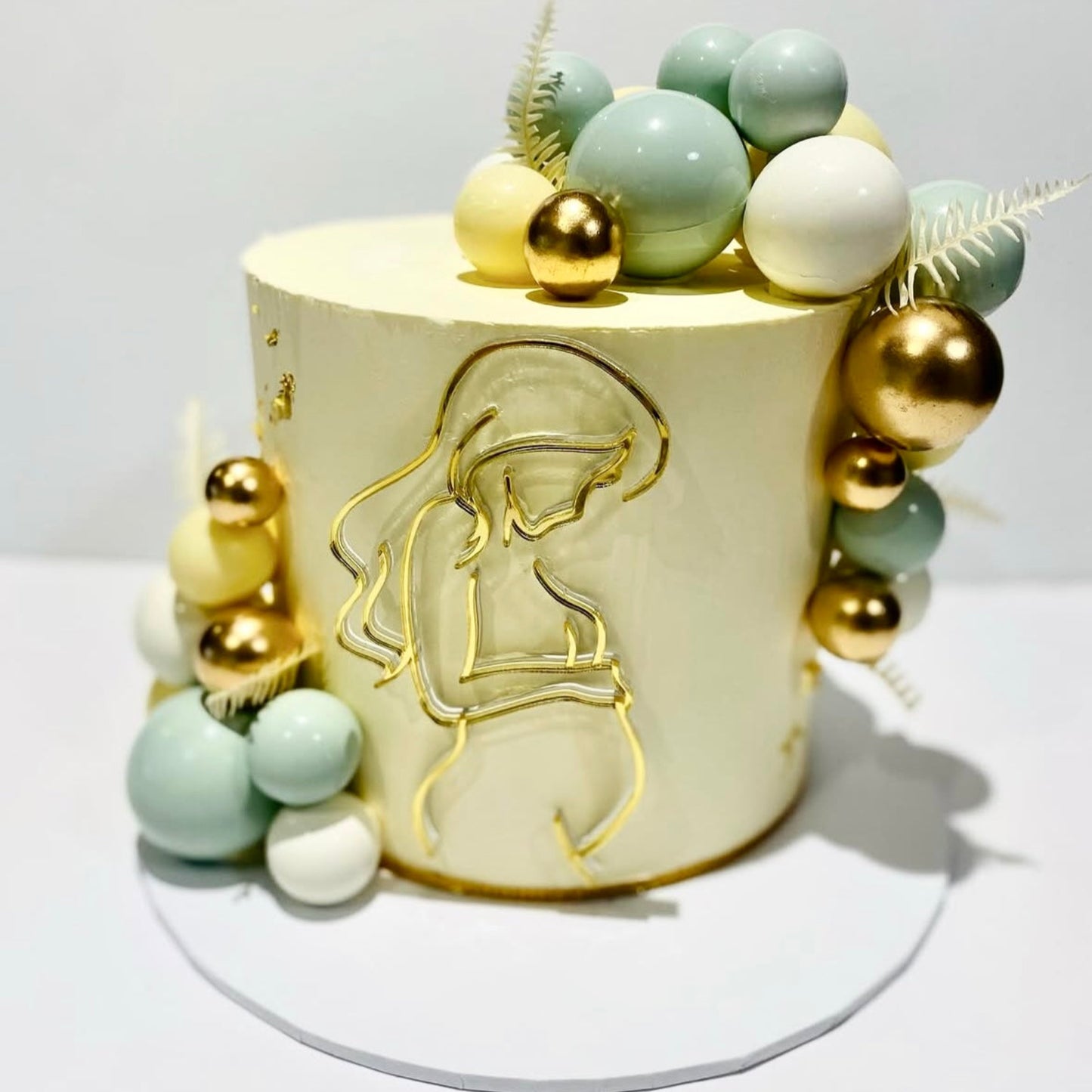 Decorative cake with gold and pastel-colored elements, with a gold line art pregnant women cake topper, on a white background