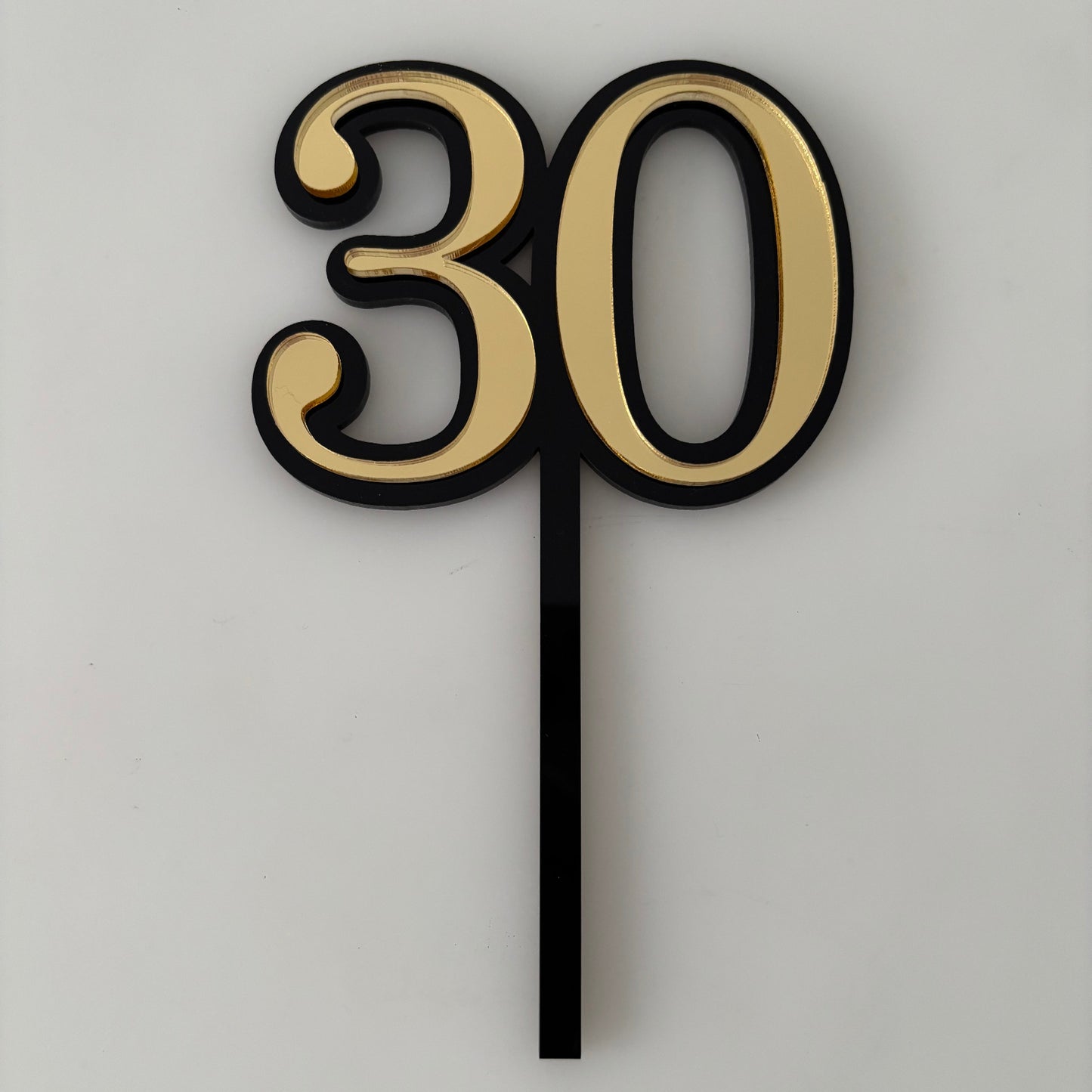 Gold cake topper with number '30' on a cake against a textured wall background