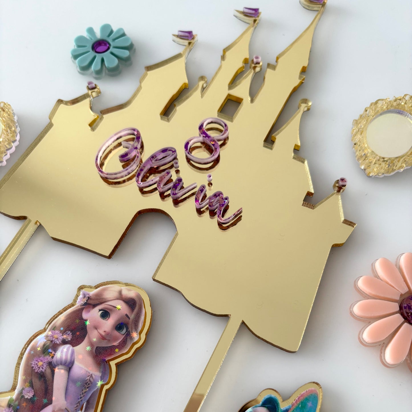 Gold castle-shaped cake topper with 'Olivia' and Disney princess design on a white background