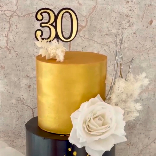 Gold cake topper with number '30' on a cake against a textured wall background