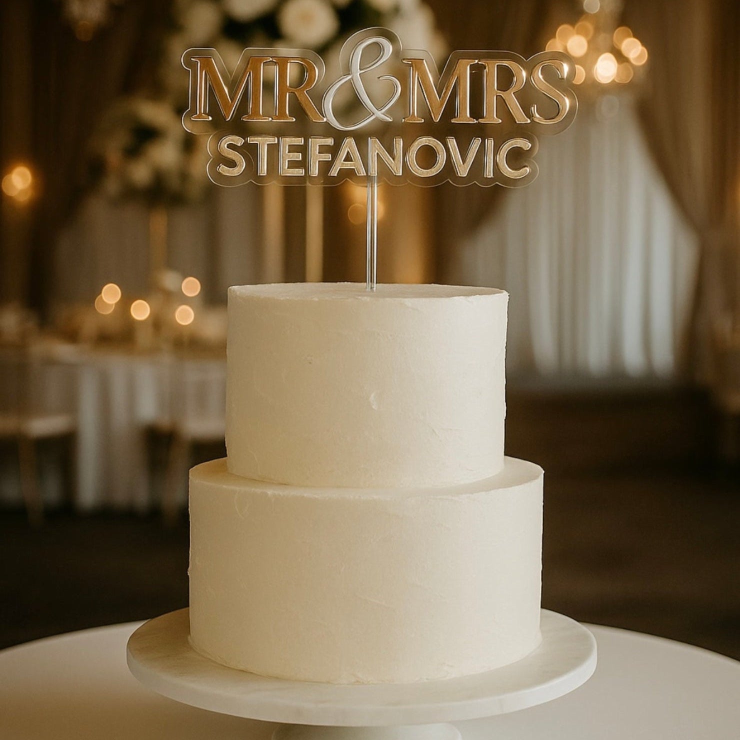 Two-tiered wedding cake with 'Mr & Mrs Stefanovic' topper in a decorated room.