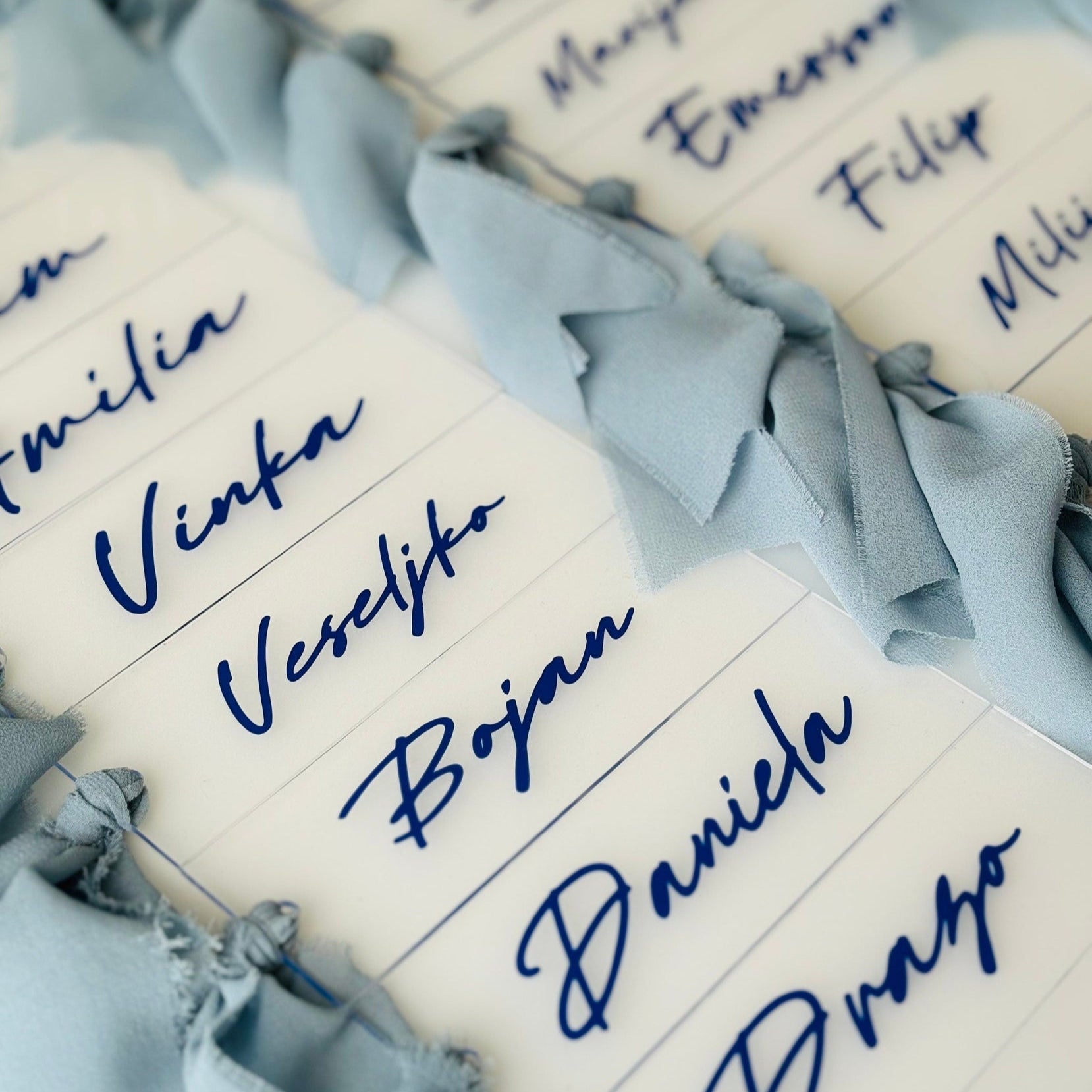 Acrylic name tags with blue text and decorative ribbons on a white background