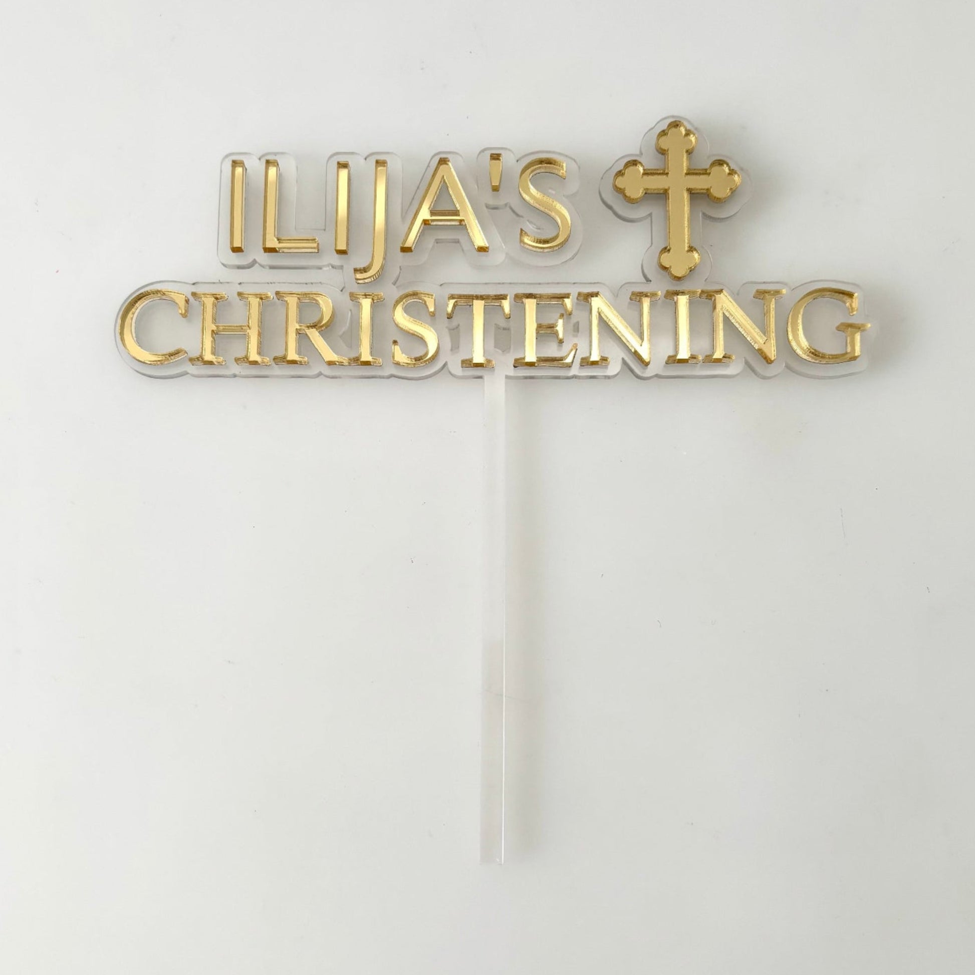 Gold christening cake topper with  personalised text and cross on a white background