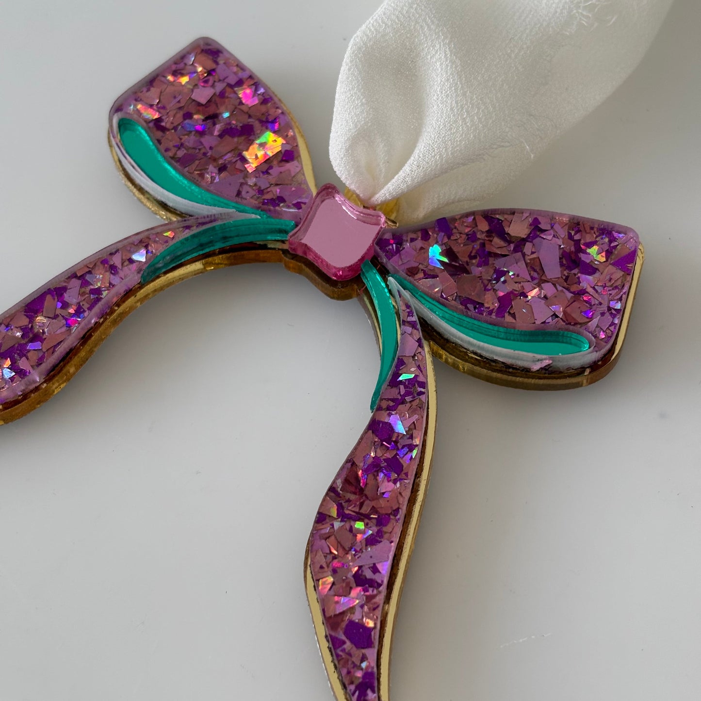Decorative bow with purple glittery  and pink acrylic enter on a white background