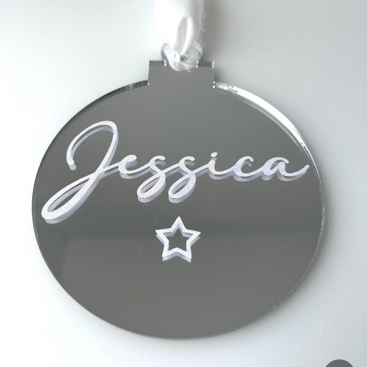 Round silver Christmas bauble with 'Jessica' and a star, hanging on a white background