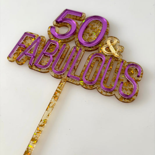 Decorative gold glitter cake topper with '50 & Fabulous' text on a white background