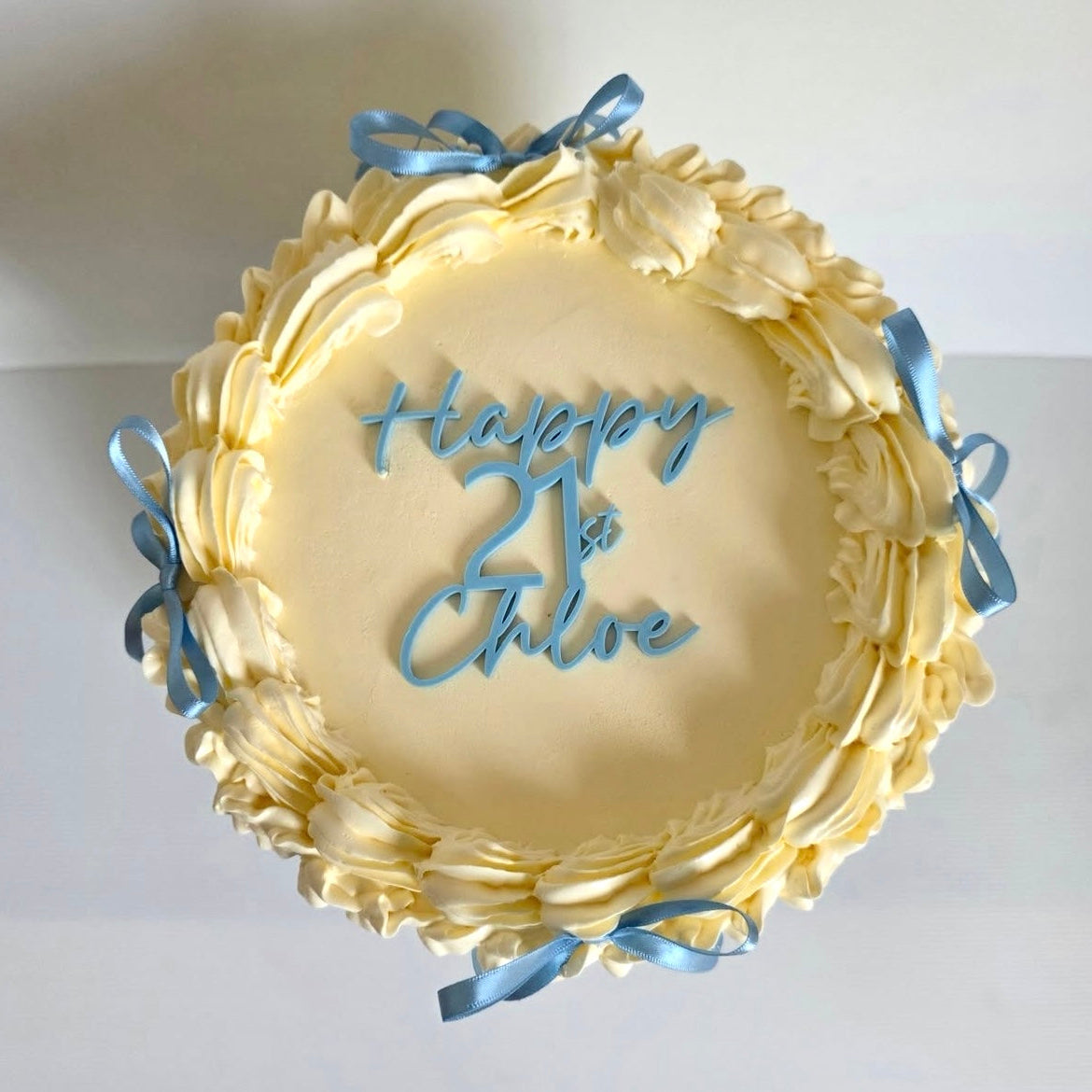Yellow cake with blue ribbons and 'Happy 1st Chloe' text on a white background