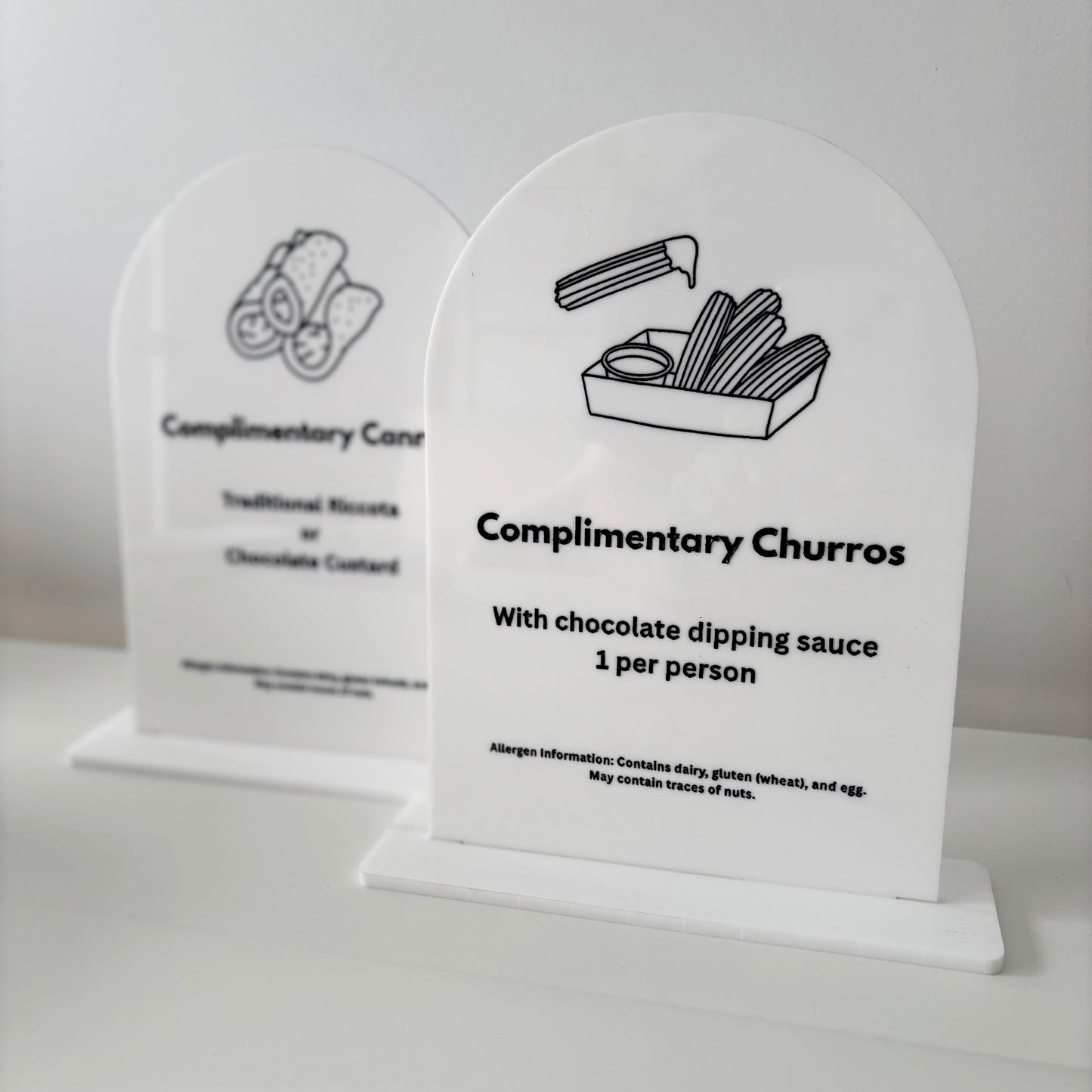 Two white acrylic signs with black text and illustrations on a light gray background