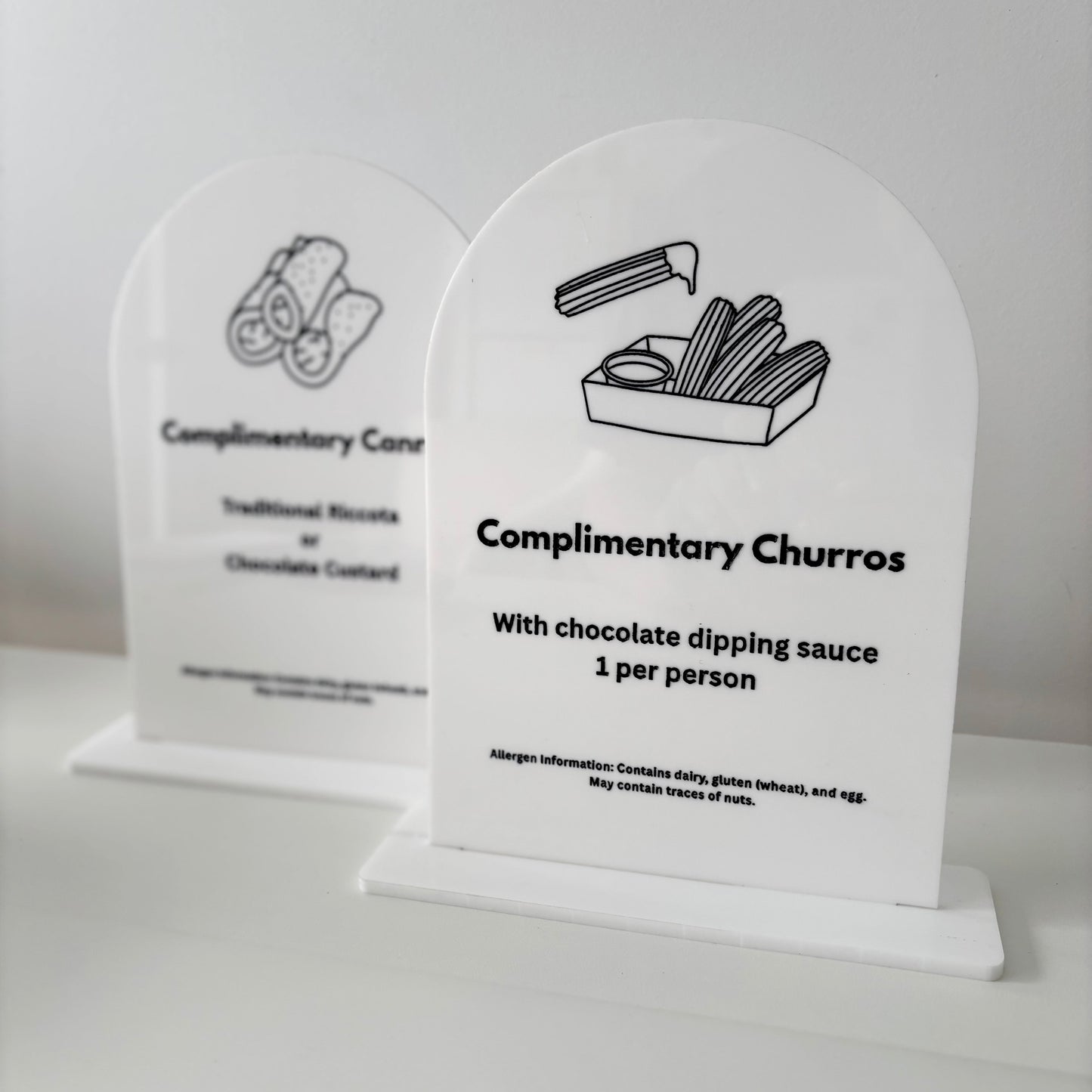 Two white acrylic signs with black text and illustrations on a light gray background