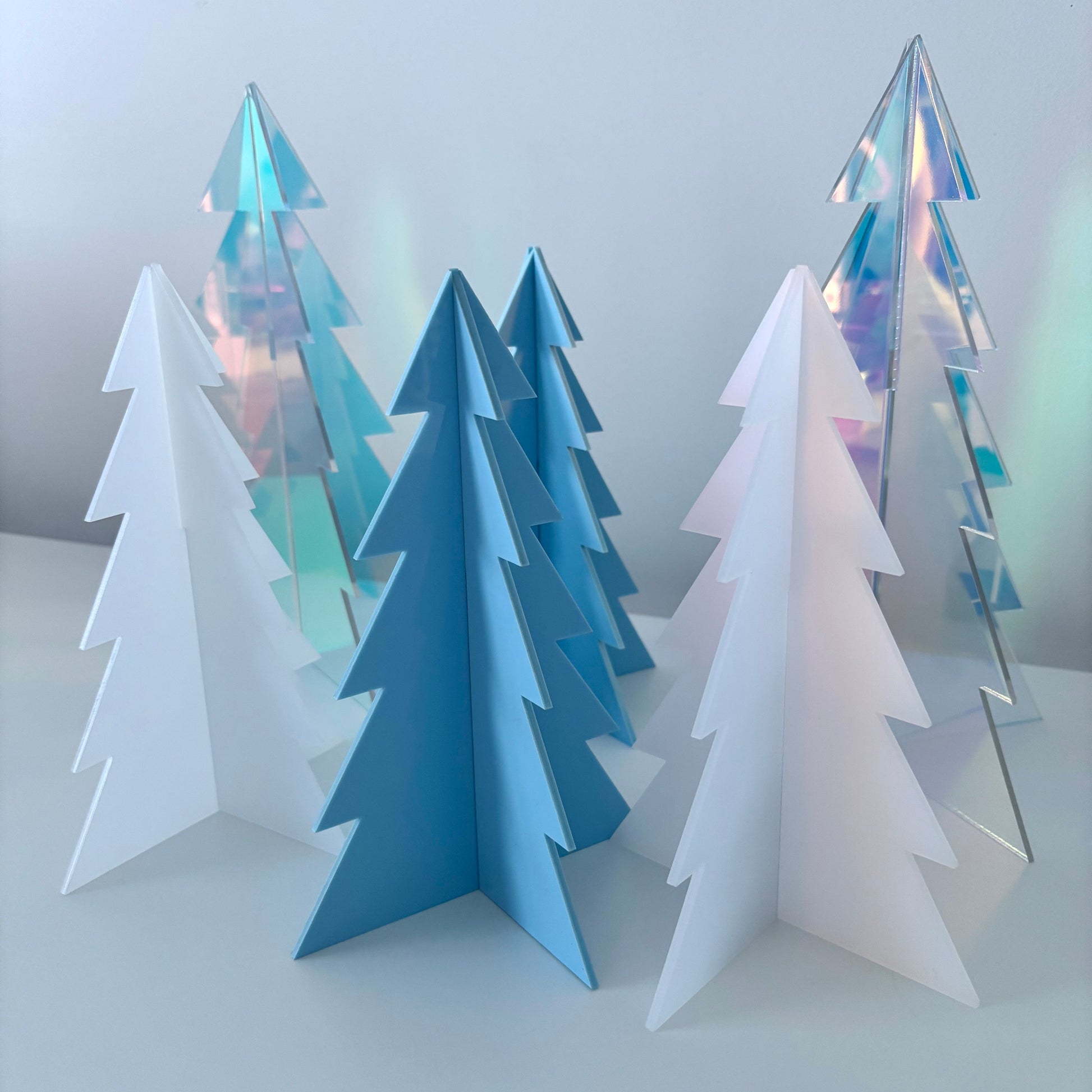 Set of acrylic Christmas trees in blue, white, and iridescent colors on a light background
