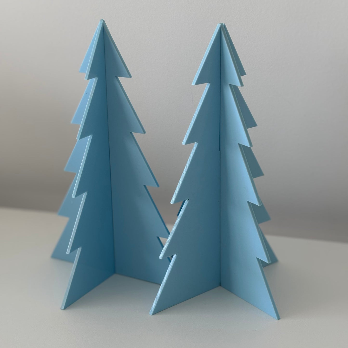 Two blue acrylic Christmas trees on a light grey background