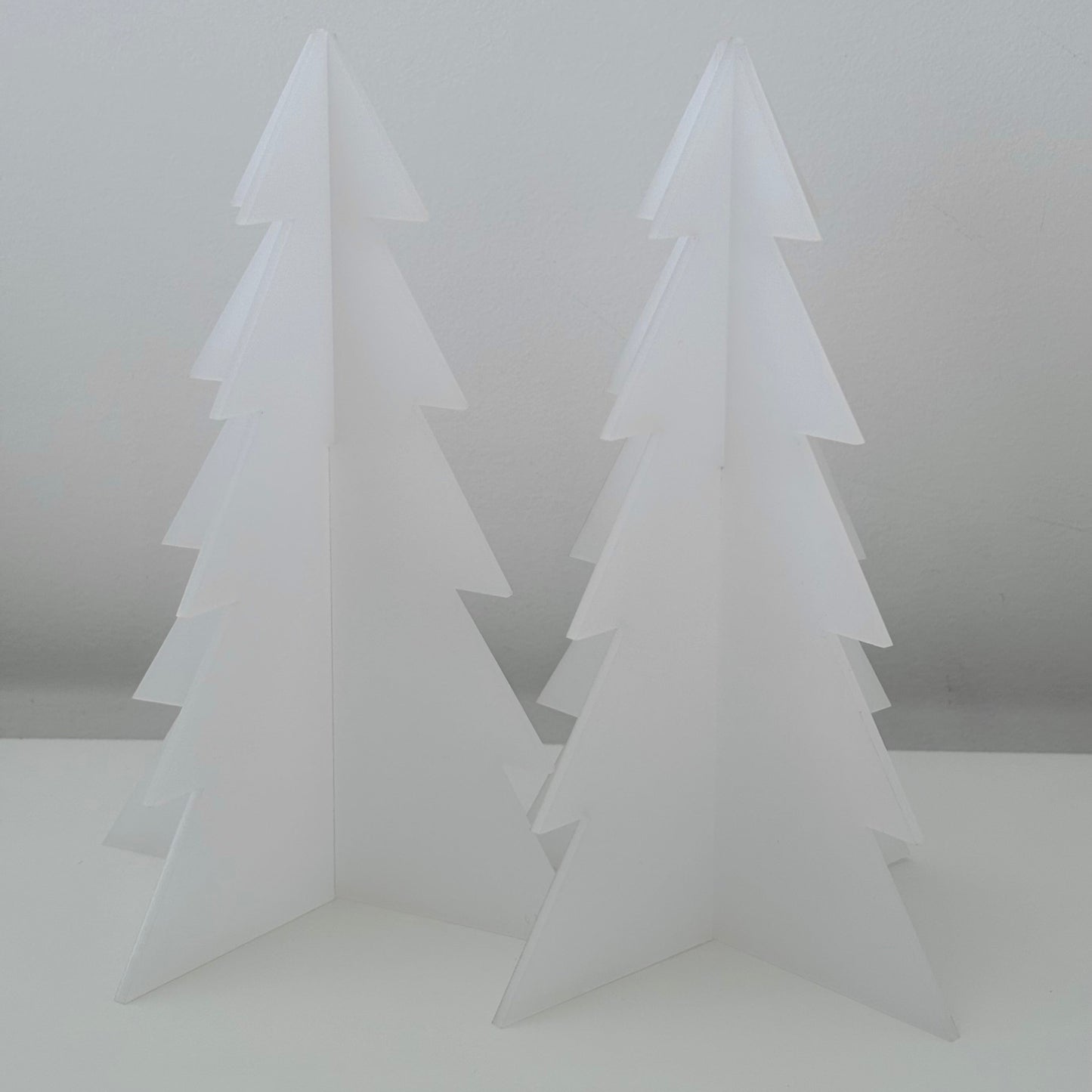 Two white acrylic Christmas trees on a light grey background