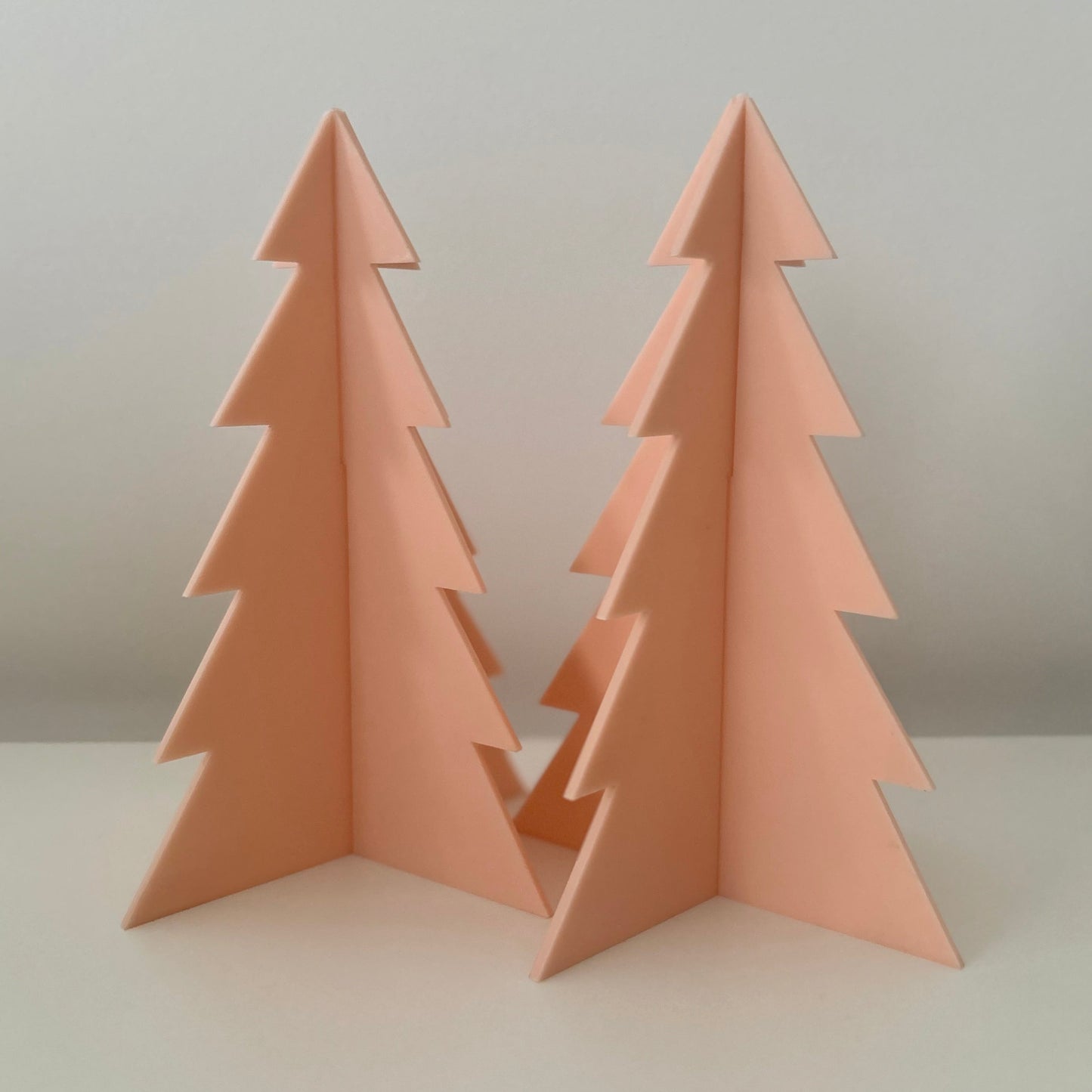 Two acrylic Christmas trees on a white surface with a light grey background