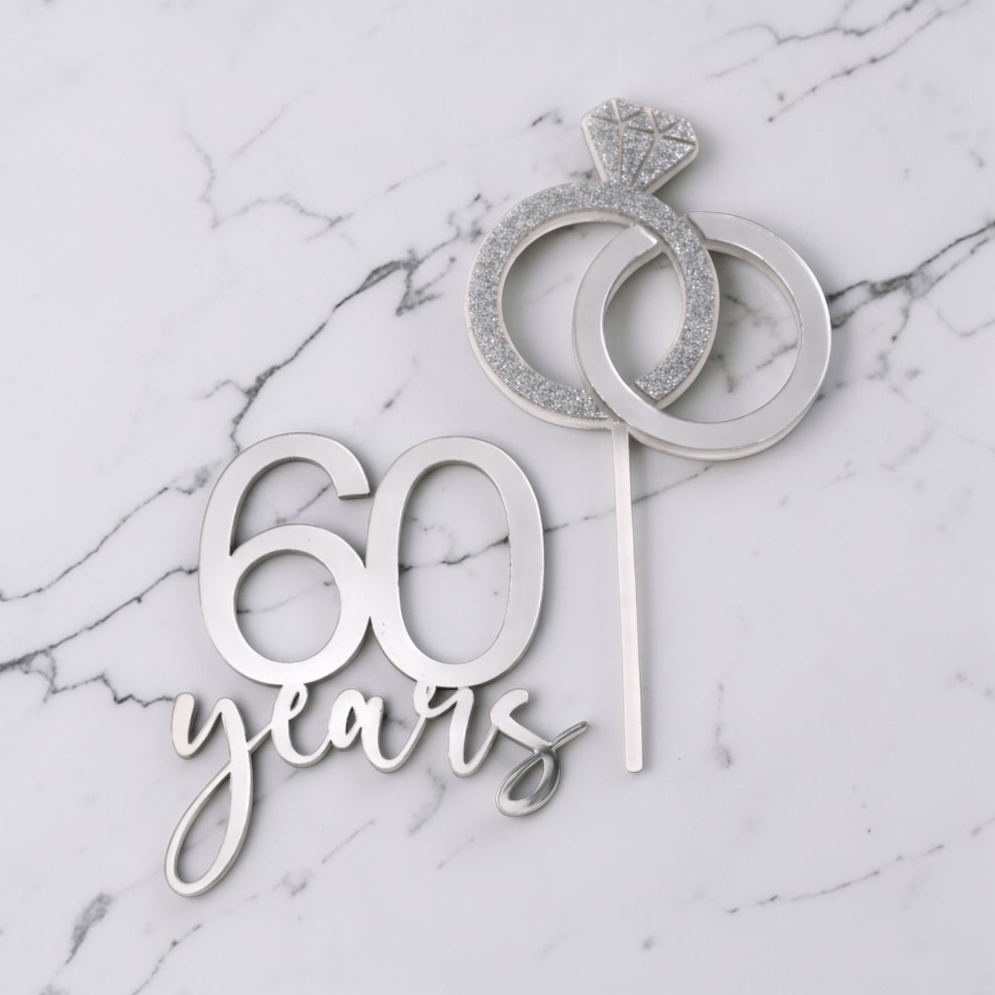 Silver cake topper with '60 years' and ring design on a marble background