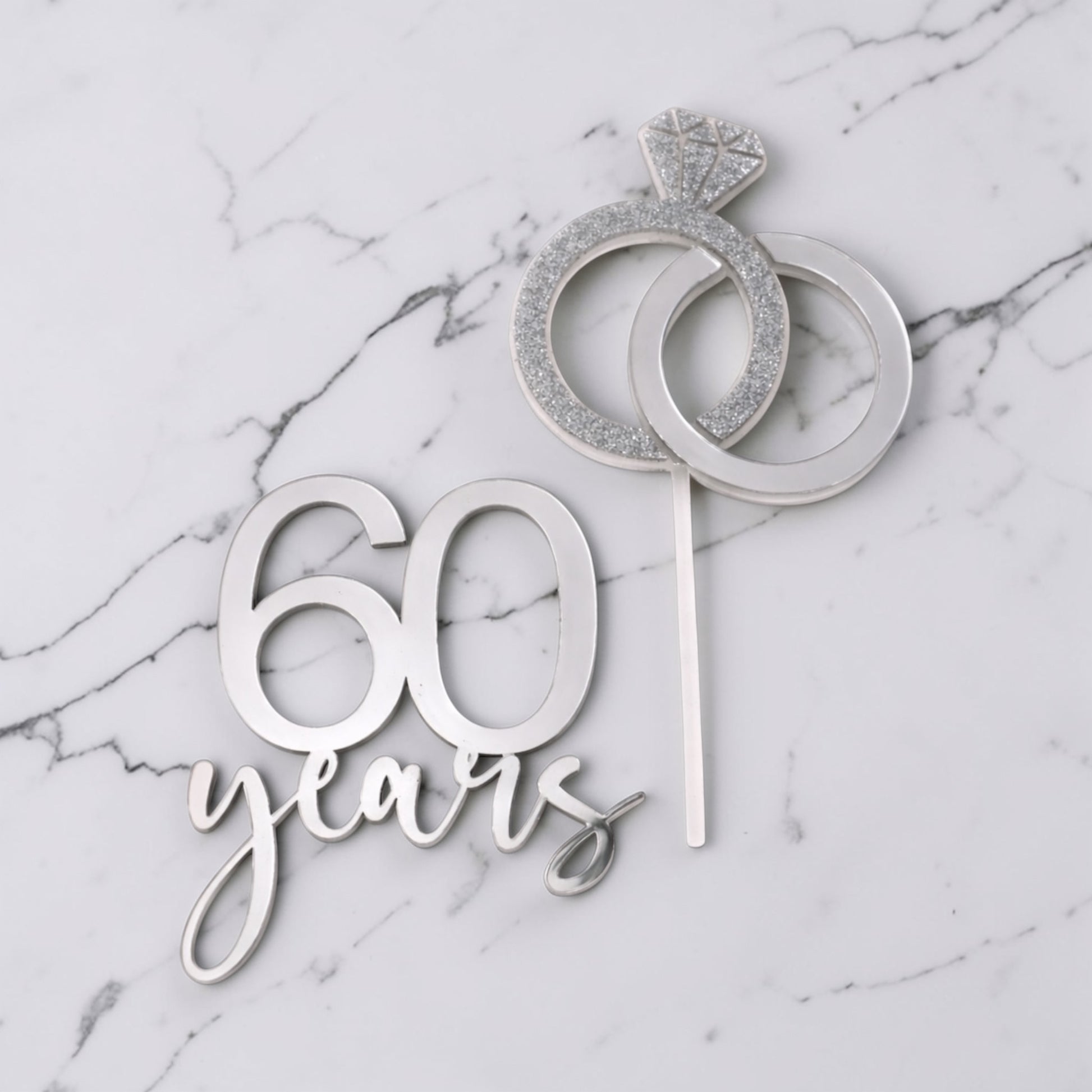 Silver cake topper with '60 years' and ring design on a marble background