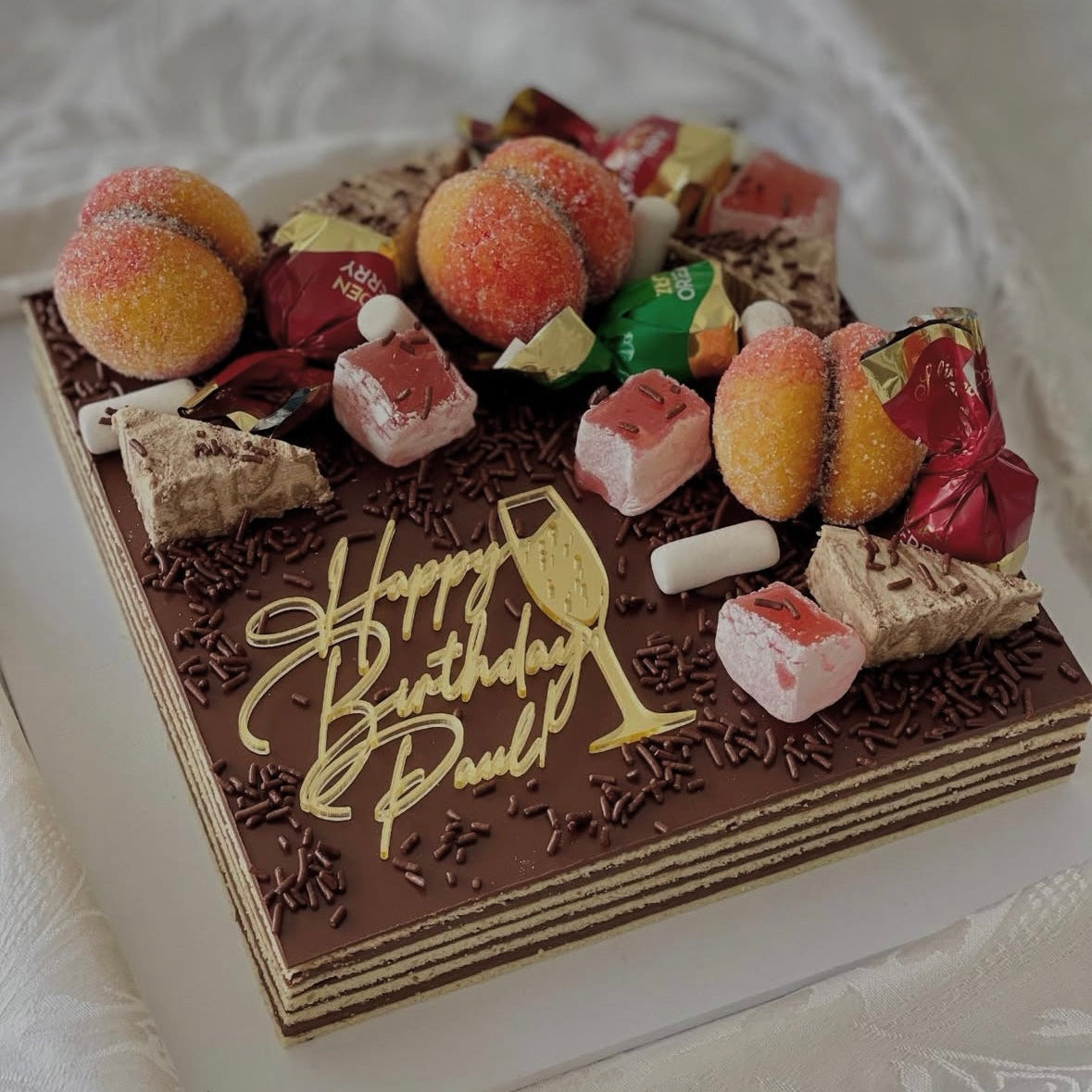 Decorative birthday cake with chocolate writing and various candies on a white background
