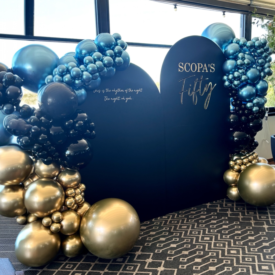 Decorative arch with blue and gold balloons and a heart-shaped sign reading 'SCOPA's Fifty'.