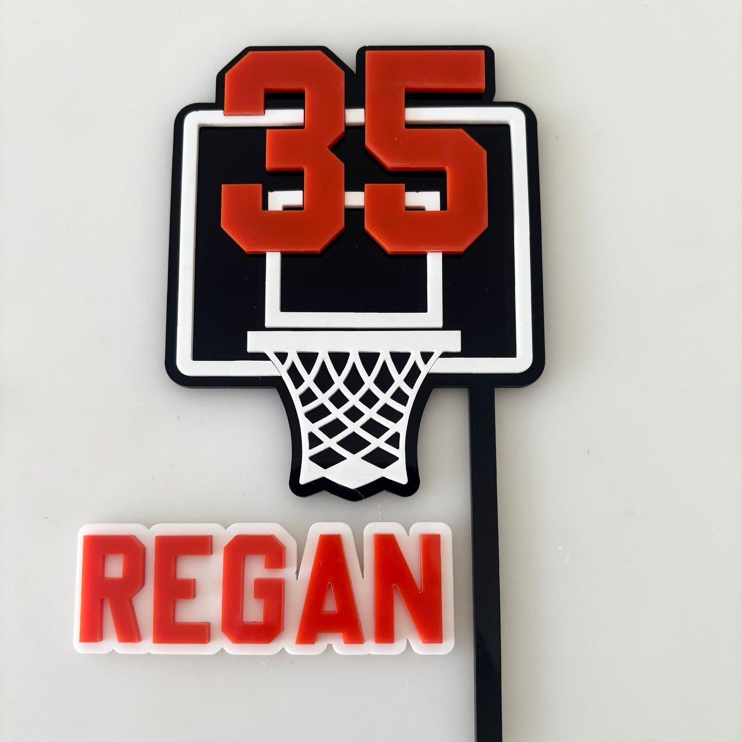 Basketball hoop with '35' and 'REGAN' text on a white background cake Topper