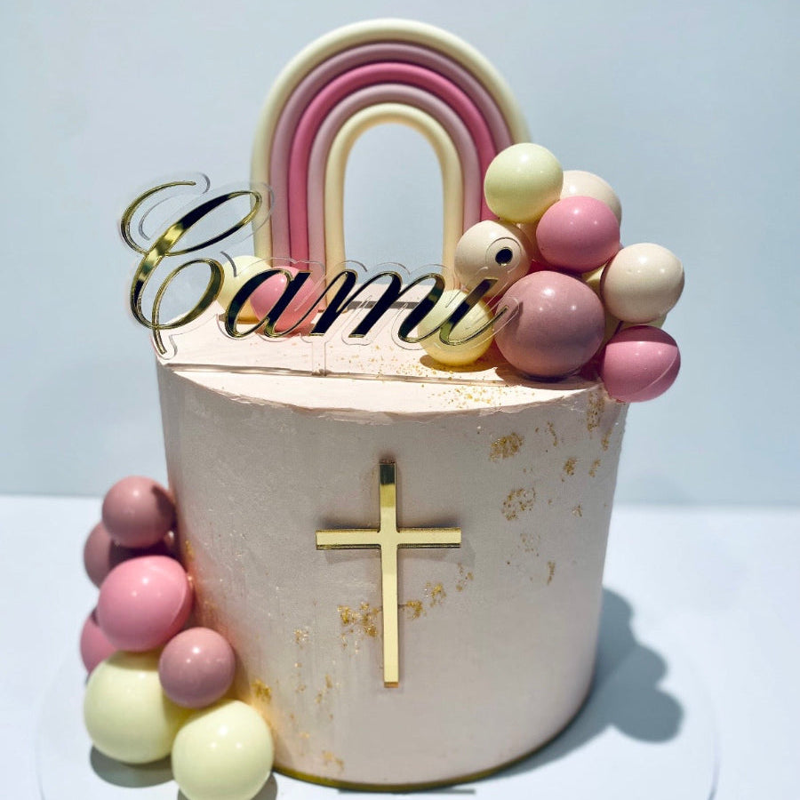 Decorative cake topper with rainbow, balloons, and cross on a white background