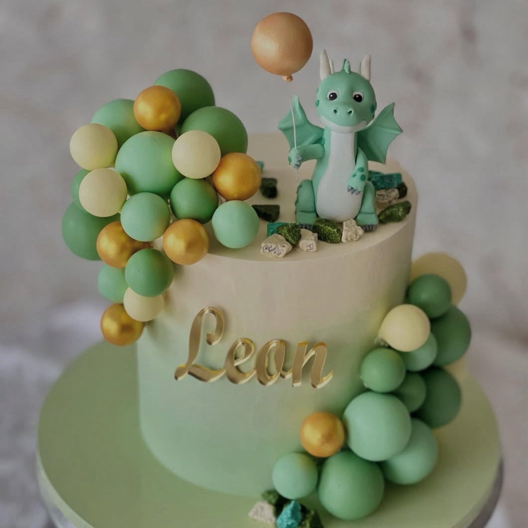 Cake with a dragon decoration and balloons, featuring the name 'Leon'.