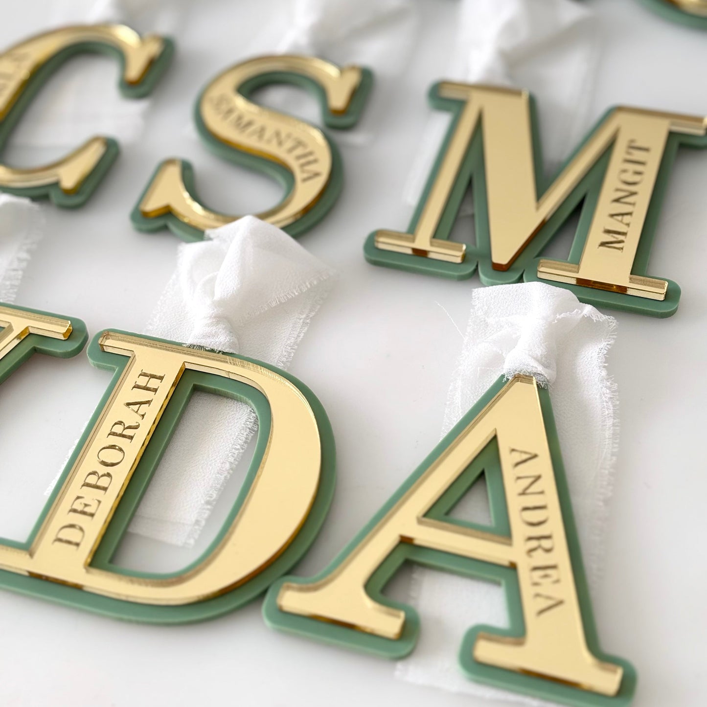 Gold and green letter-shaped objects with names engraved on them, on a white background.