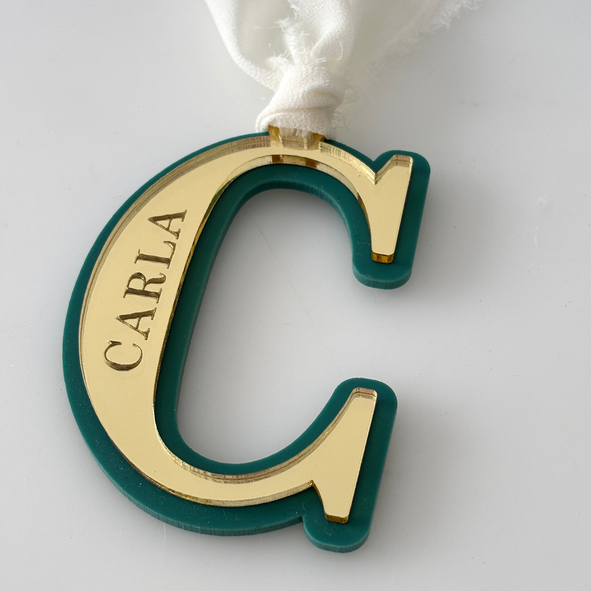 Gold and green letter 'C' ornament with 'CARLA' engraving on a white background