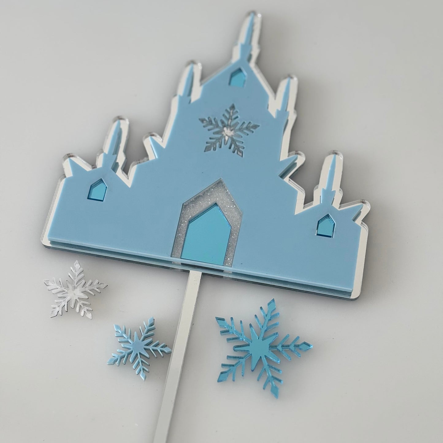 Blue disney frozen castle-shaped cake topper with snowflakes on a grey background
