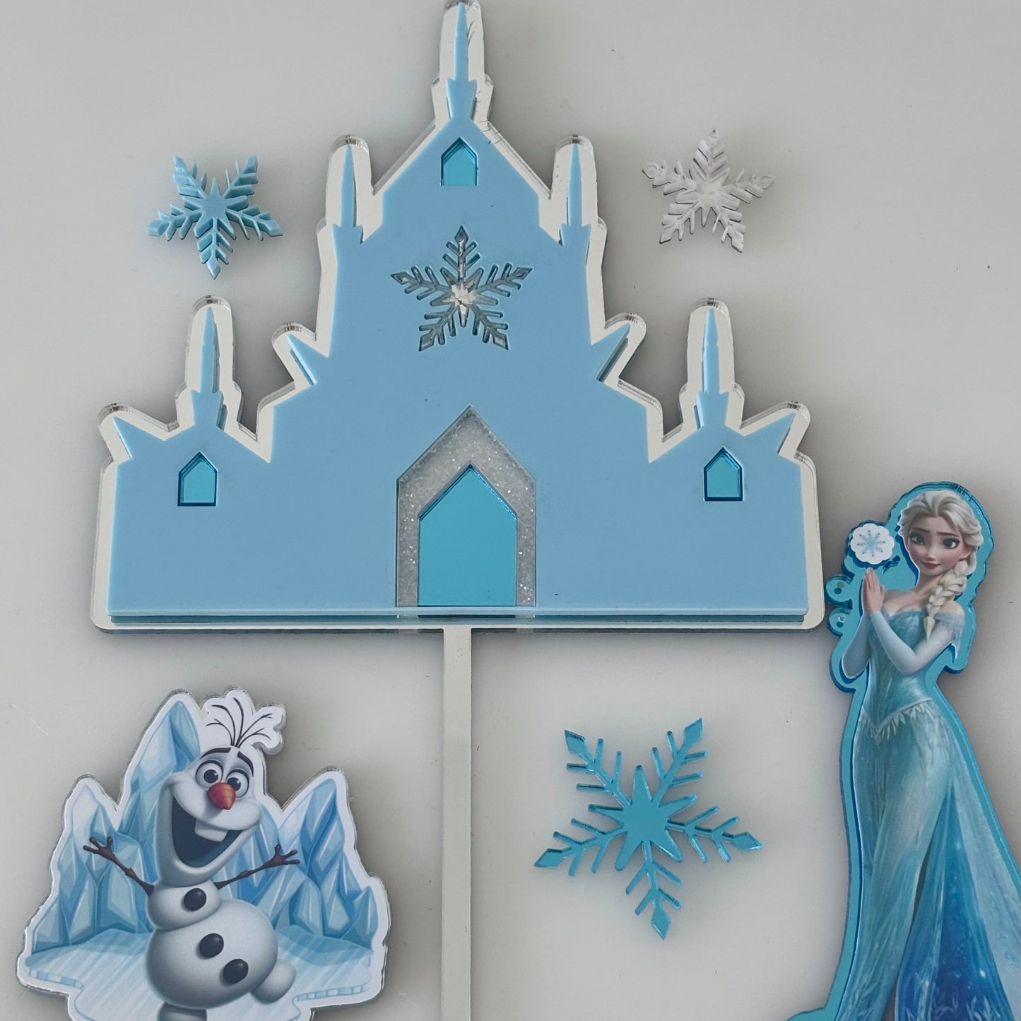 Frozen Cake Topper set with a castle, Elsa, Olaf, and snowflakes on a grey background