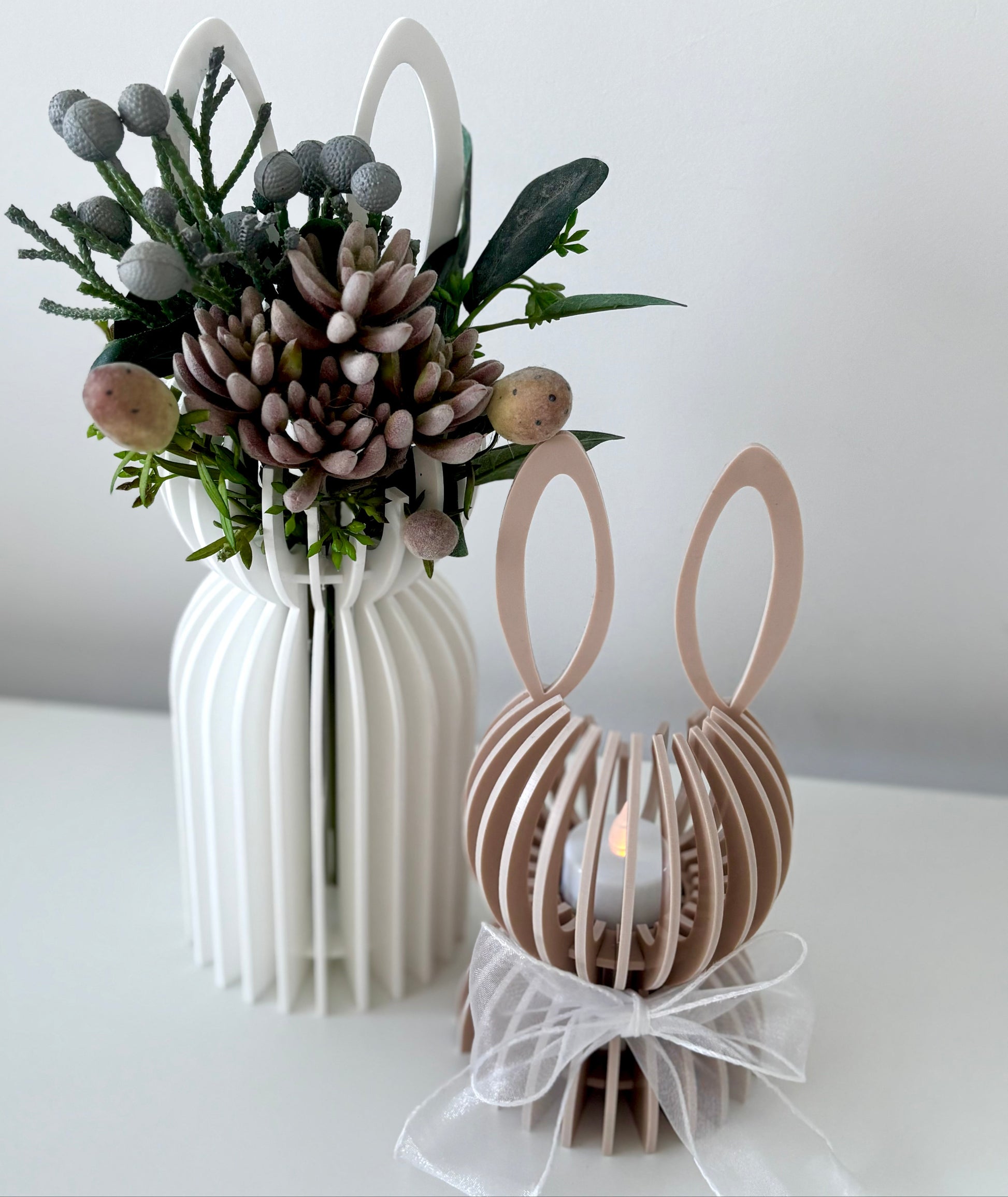 Decorative vase with floral arrangement and a candle holder shaped like bunny ears on a white surface.