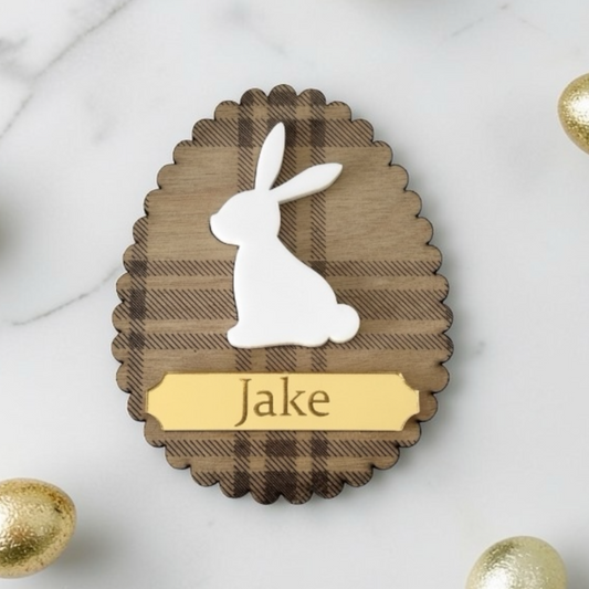 Wooden Easter Placecard with a white rabbit silhouette and 'Jake' engraving on a marble surface with gold eggs.