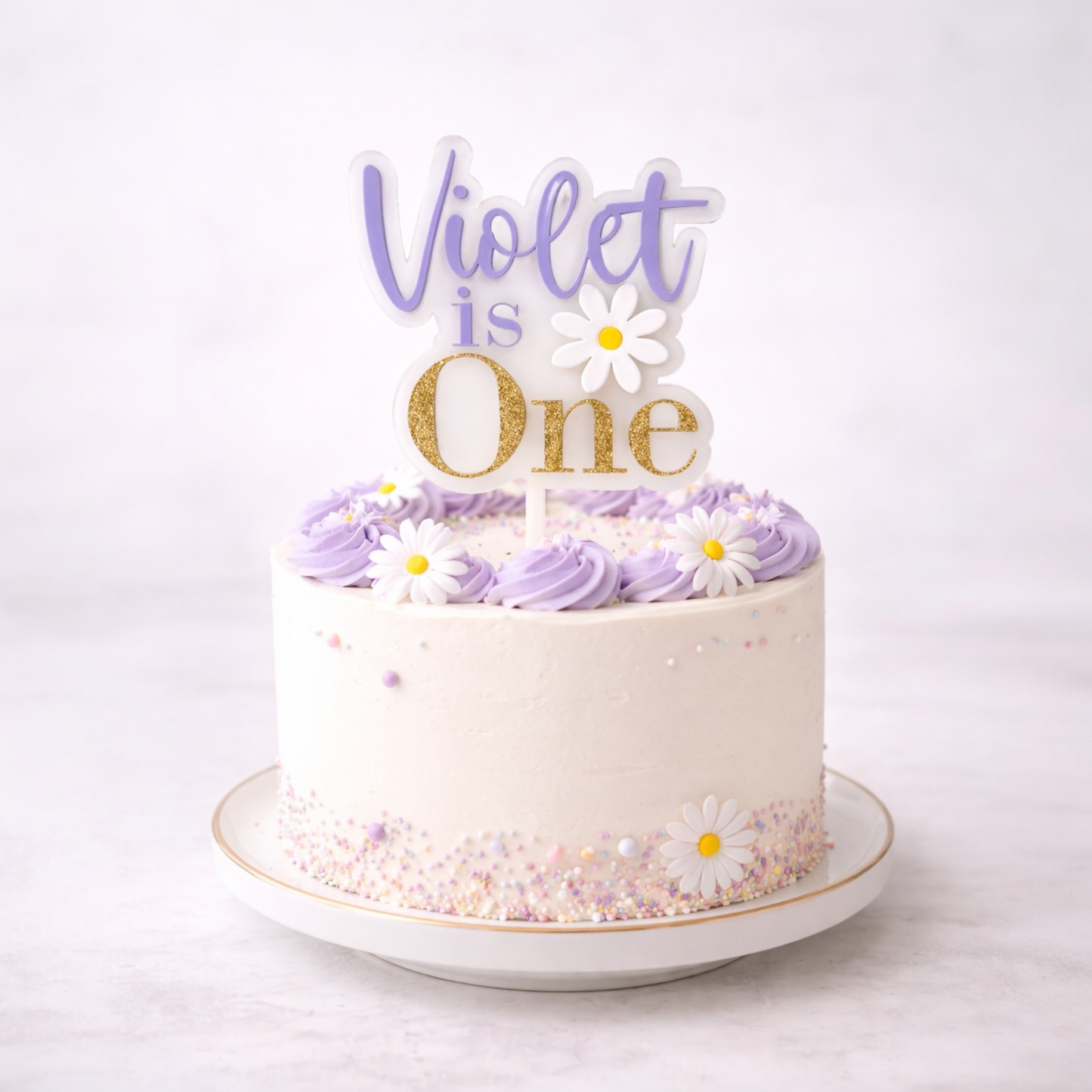 White cake with purple frosting and 'Violet is One' topper on a white background