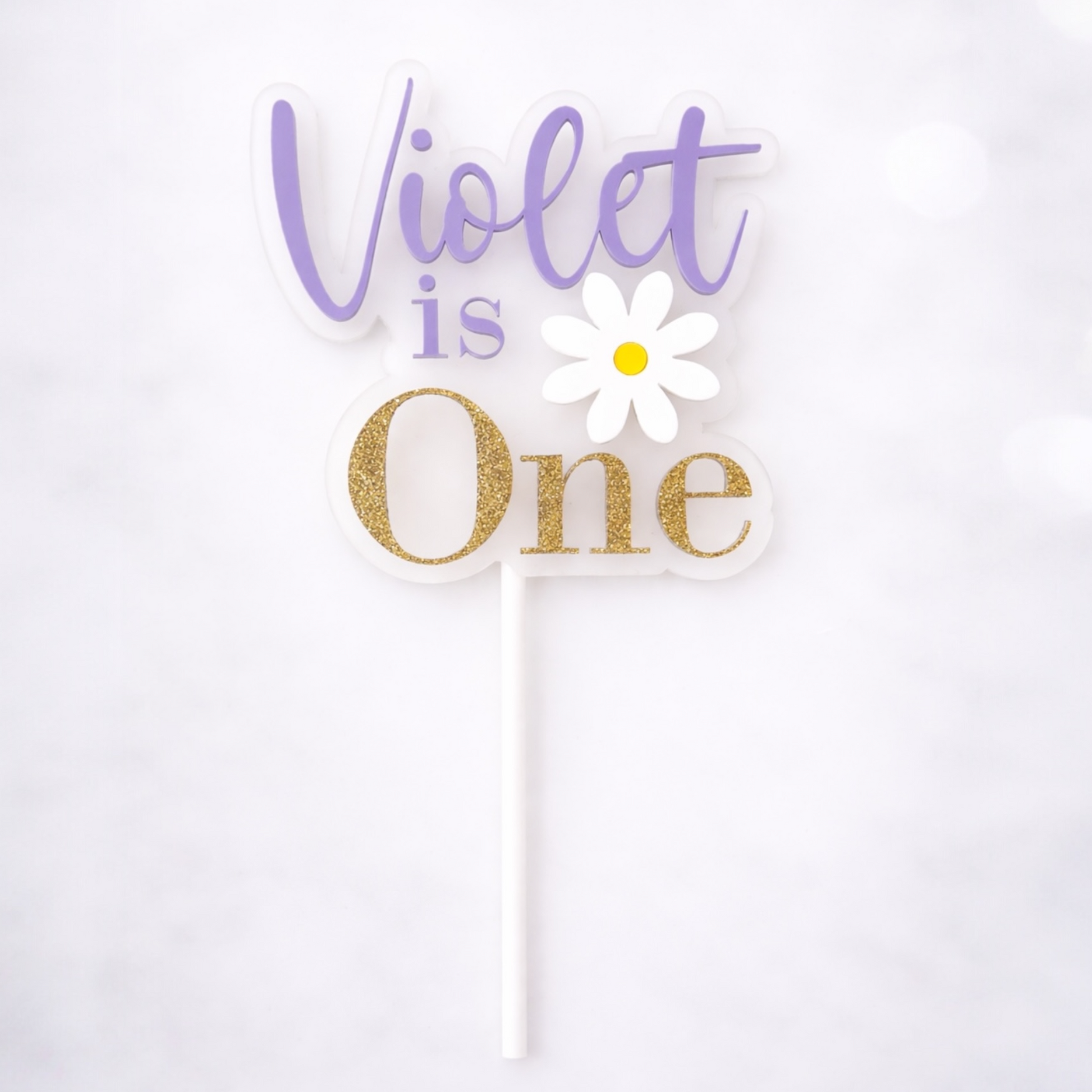 Cake topper with 'Violet is One' text and a daisy on a white background