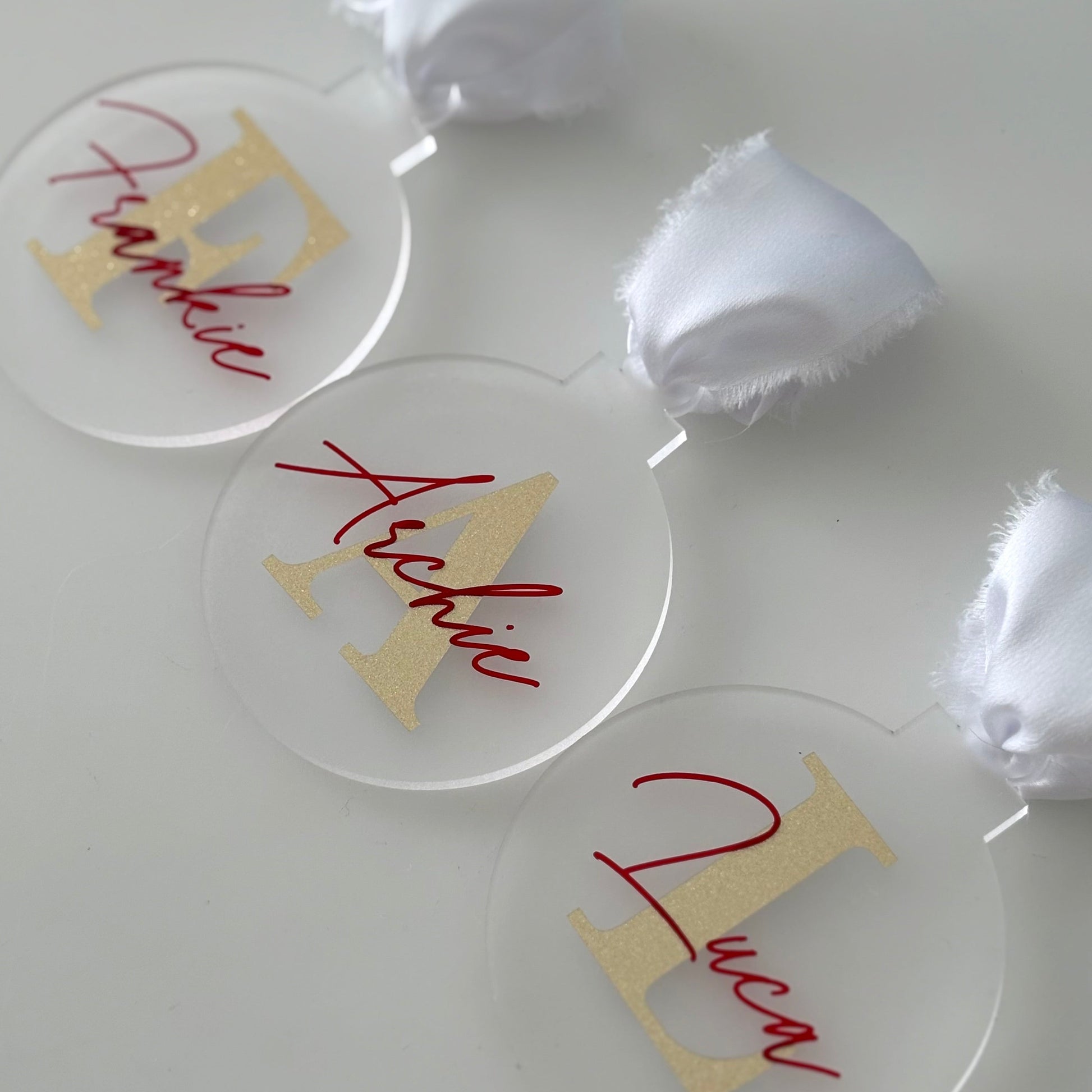 Clear circular christmas baubles with gold and red text on a white surface.