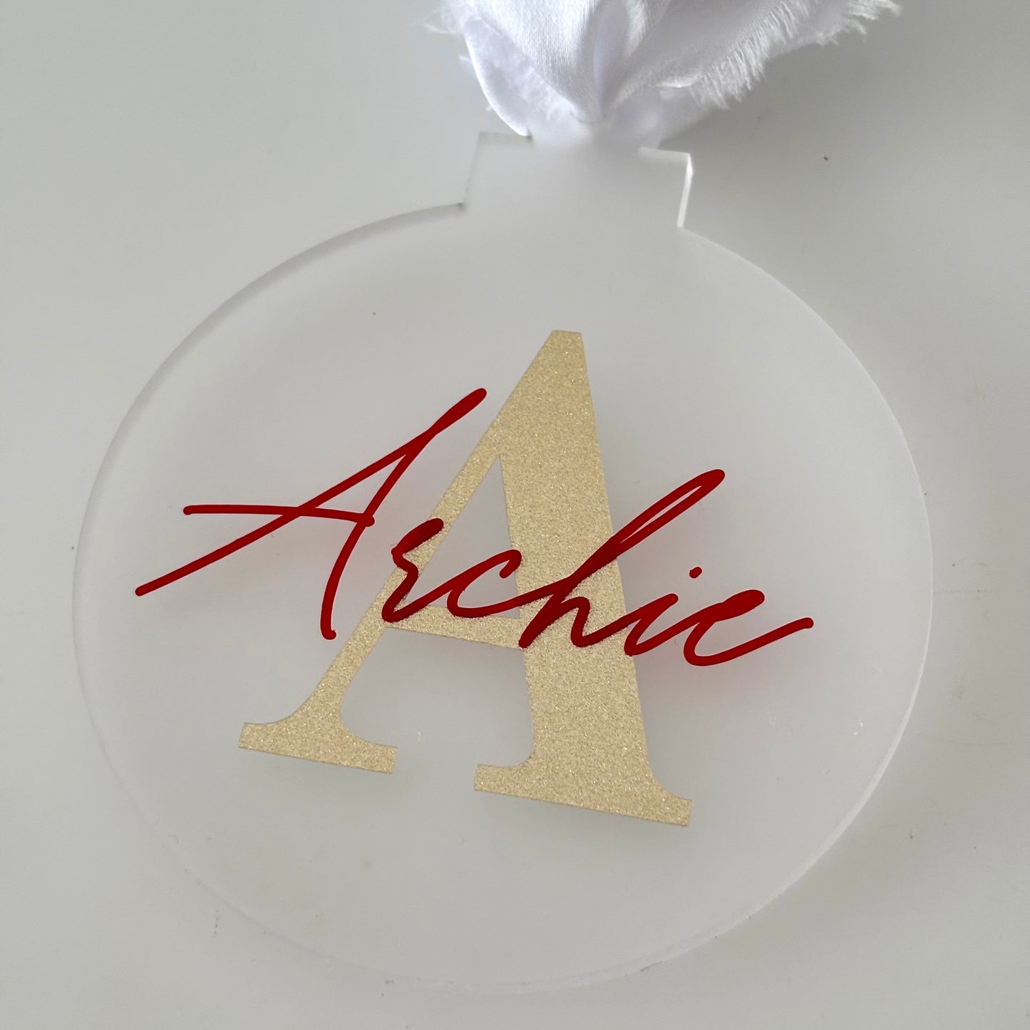 Clear acrylic ornament with gold letter 'A' and red name 'Archie' on a white background