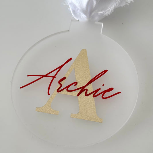 Clear acrylic ornament with gold letter 'A' and red name 'Archie' on a white background