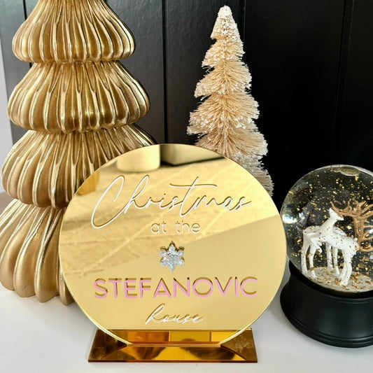 Gold Christmas ornament with 'Christmas at the Stefanovic Home' text, gold tree, and snow globe with deer on a black background.