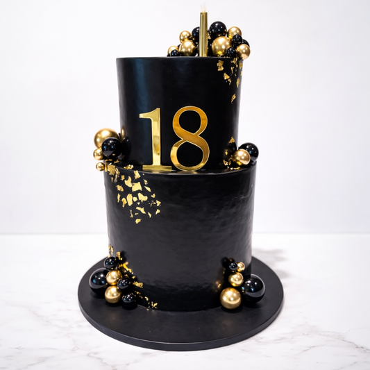 Black cake with gold number cake topper decorations and number 18 on a white background
