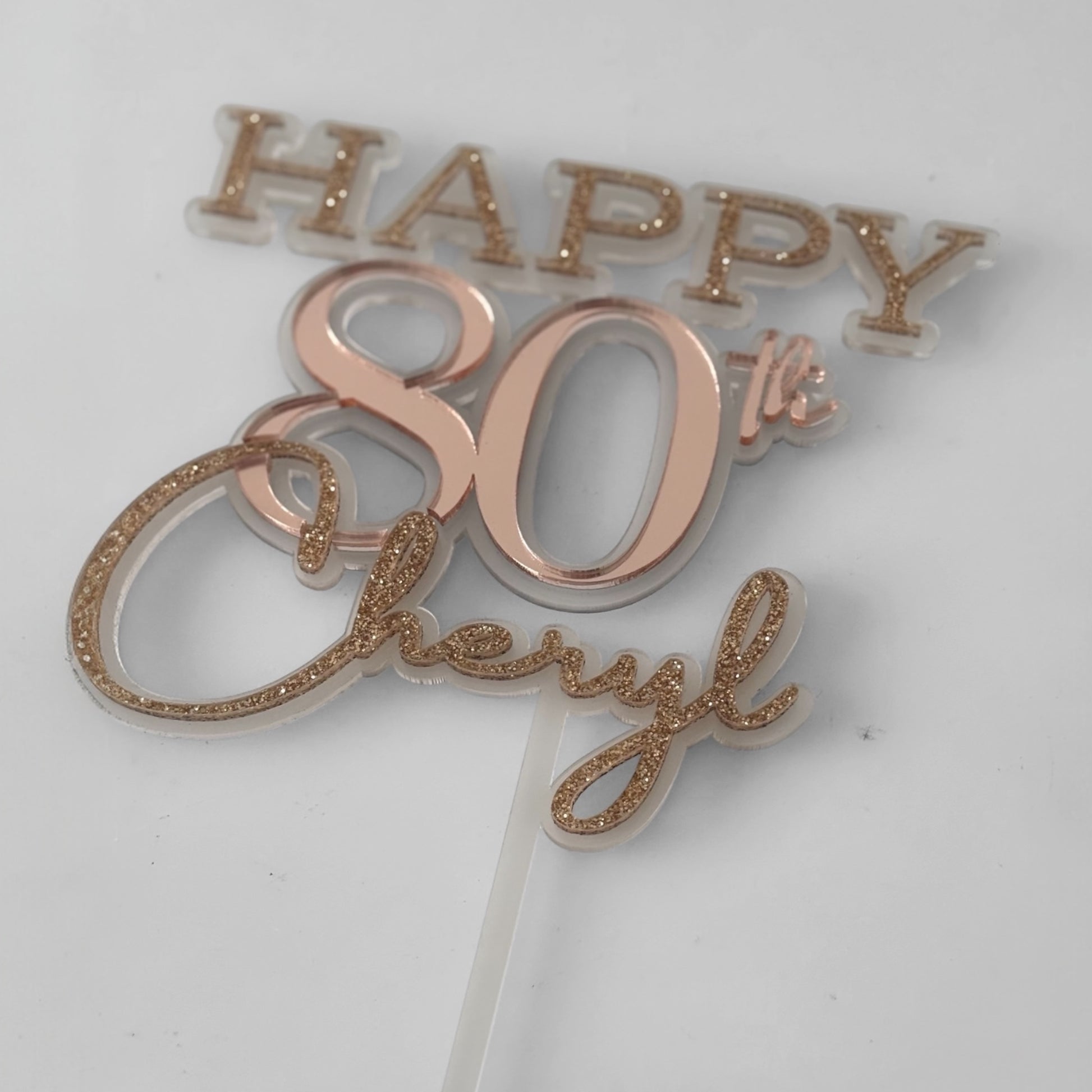 Rose gold 'Happy 80th' cake topper on a white background
