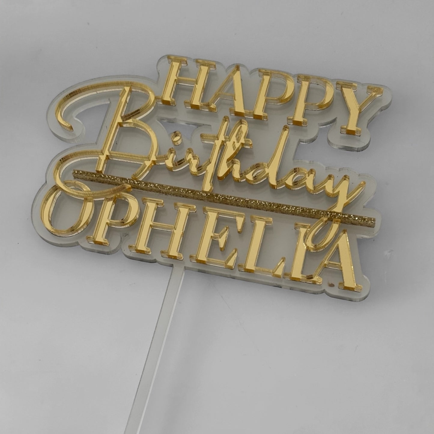 Gold 'Happy Birthday Ophelia' cake topper on a white background