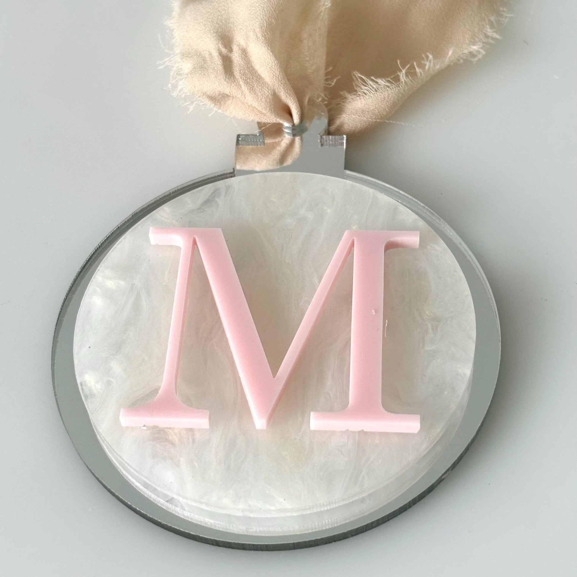 Decorative Christmas bauble with pink letter 'M' on a light marbled background
