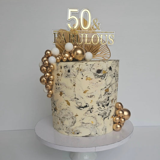 Decorative cake with gold accents and '50 & Fabulous' cake topper on a white background
