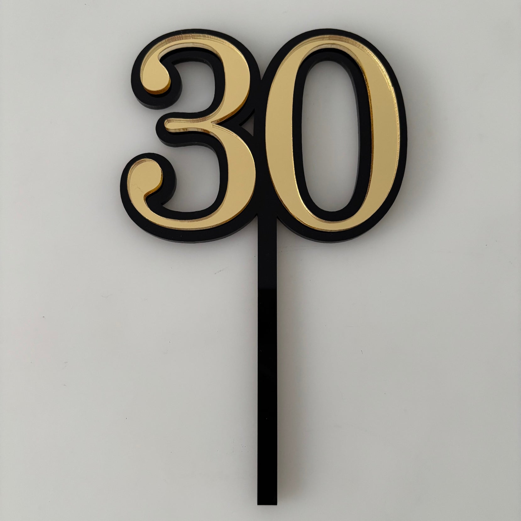Gold cake topper with number '30' on a cake against a textured wall background
