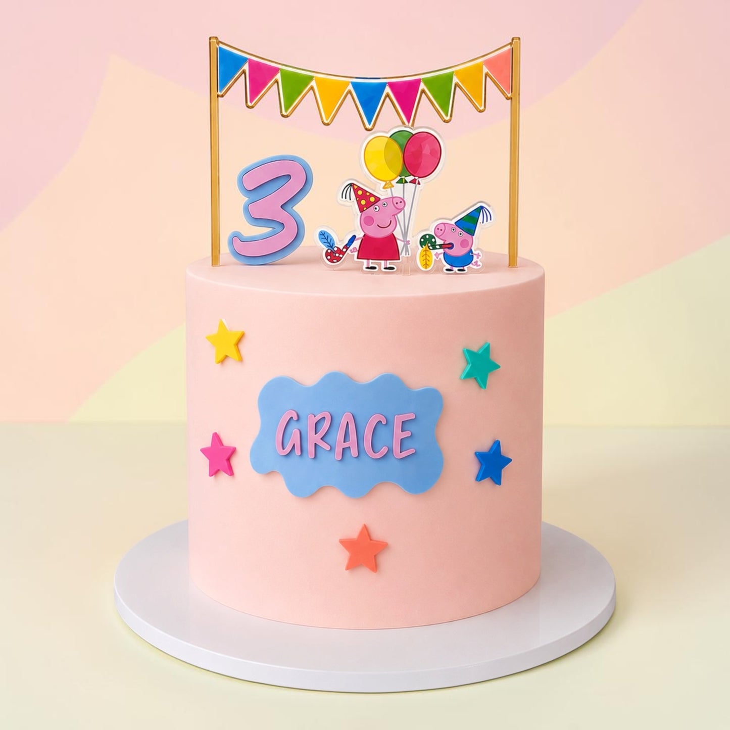 A pink frosted birthday cake on a white round base, decorated with a blue cloud-shaped nameplate reading 'GRACE', colorful stars, and a festive topper featuring a large number 3, Peppa Pig characters, and balloons under a bunting banner.