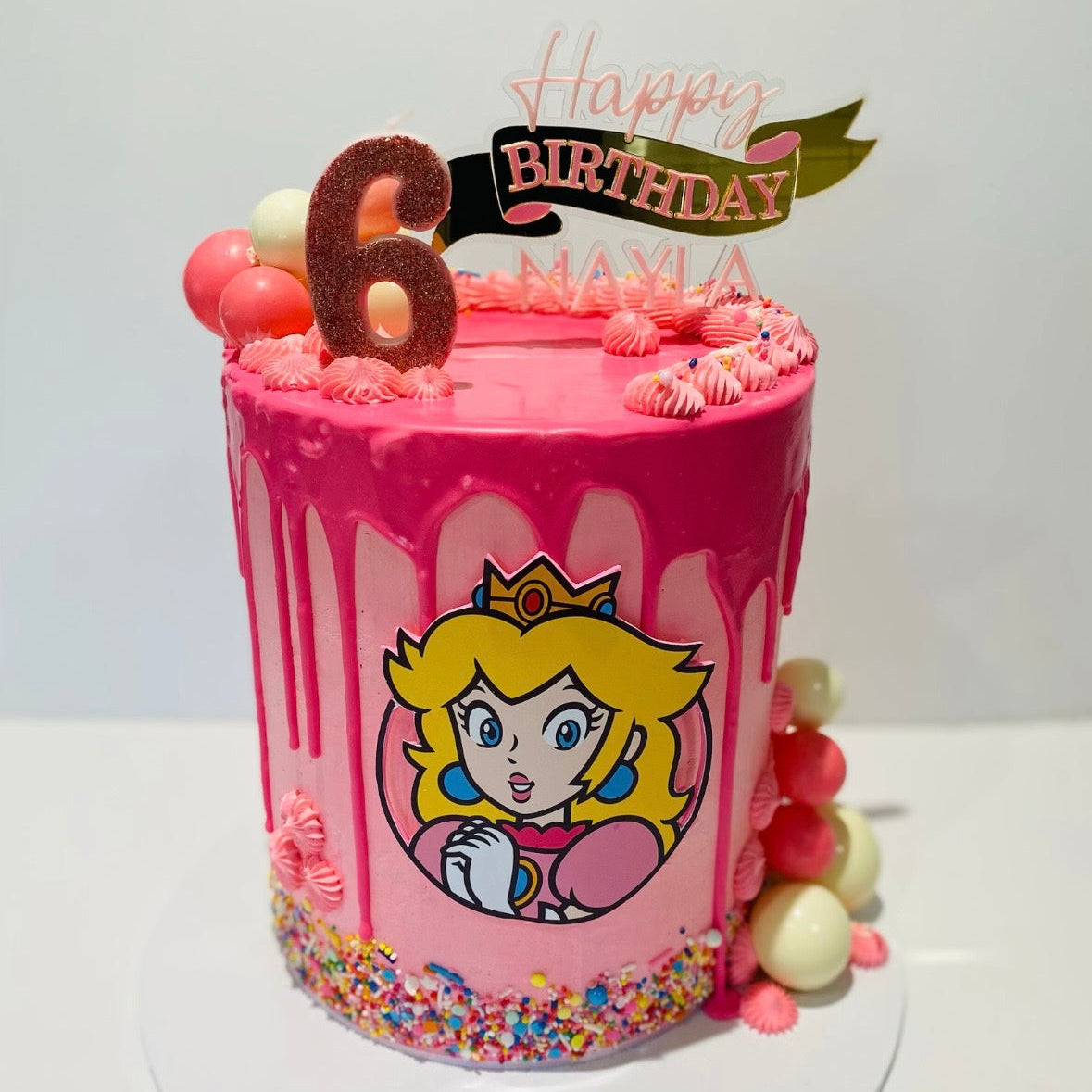 Pink birthday cake with Princess Peach and 'Happy Birthday' topper on a white background